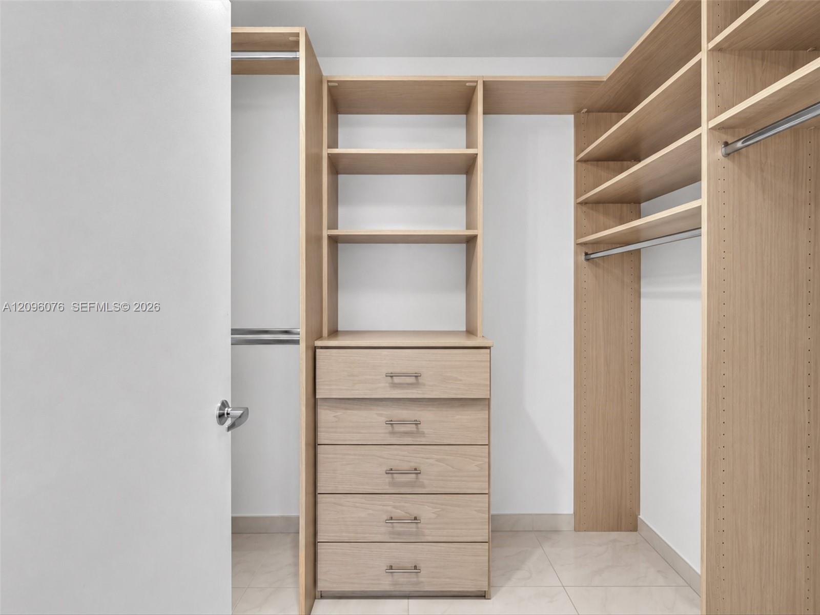 Custom walk-in closet featuring light-toned wood-finish cabinetry, built-in shelving, integrated dresser drawers, and metal hanging rods