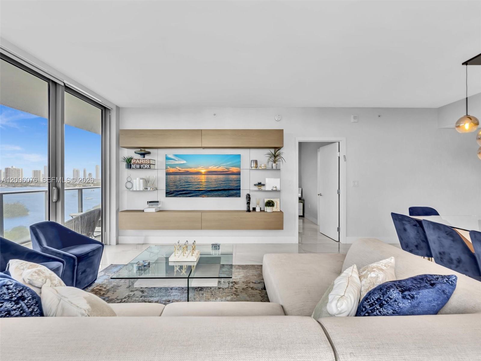 Living area featuring floor-to-ceiling glass panel doors, custom built-in wood-finish cabinetry, neutral stone-finish flooring, and pendant lighting