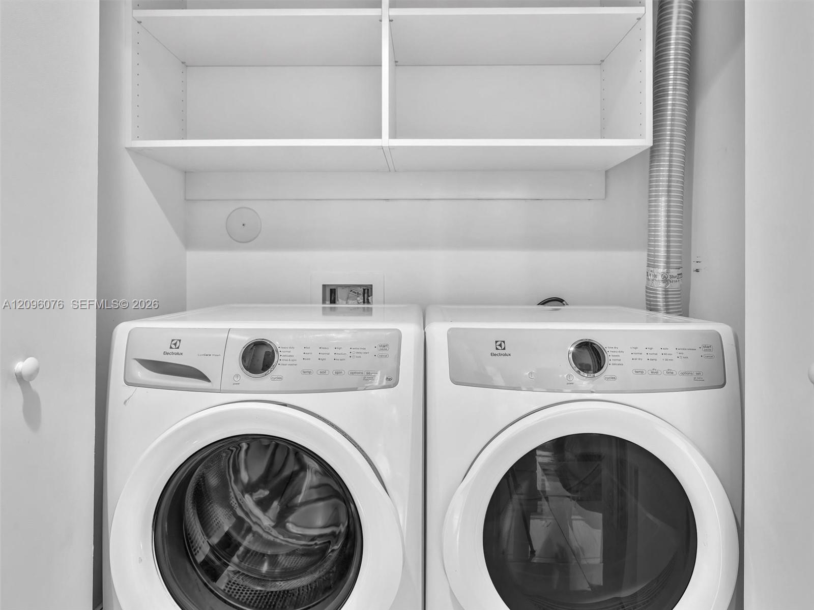 Laundry space featuring stacked white custom shelving and side-by-side front-loading appliances
