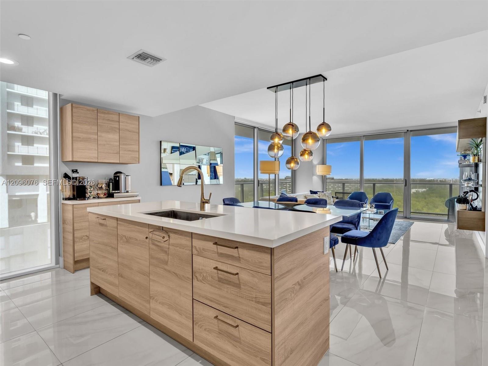 Kitchen island with wood-finish cabinetry, white countertop, undermount sink, and bronze-tone faucet, complemented by floor-to-ceiling windows and a multi-pendant light fixture