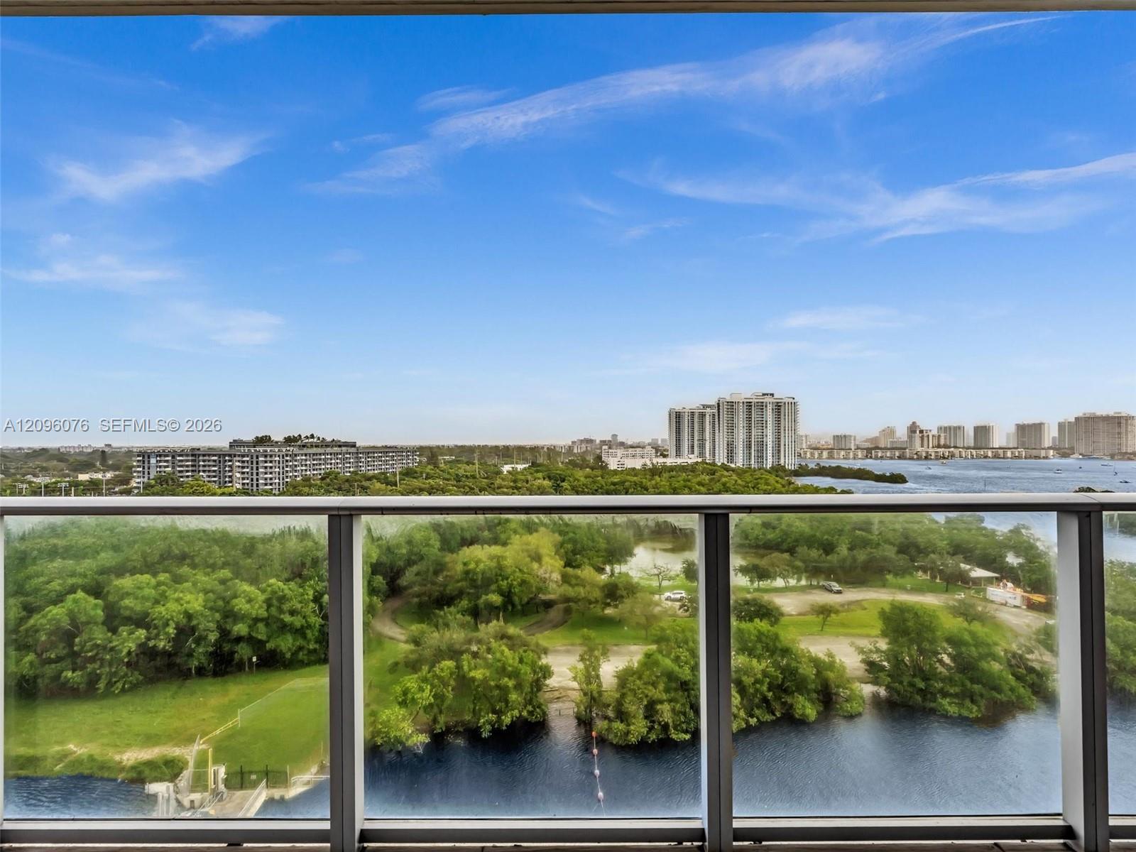 Balcony featuring glass panel railing and panoramic landscape, waterway, and skyline scenery