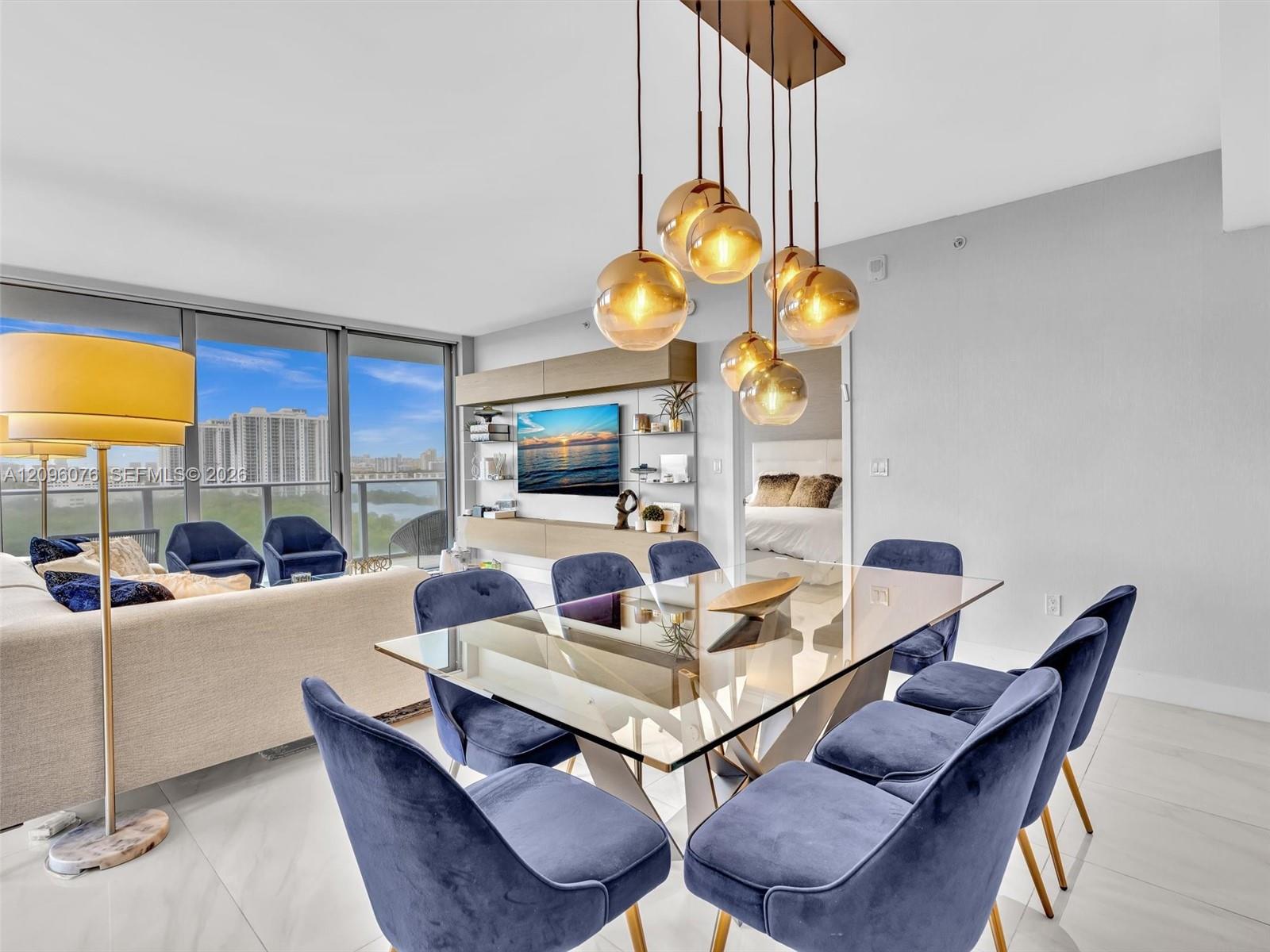 Open-concept living space featuring expansive floor-to-ceiling windows, polished stone-finish flooring, custom built-in media cabinetry, and a modern multi-pendant light fixture