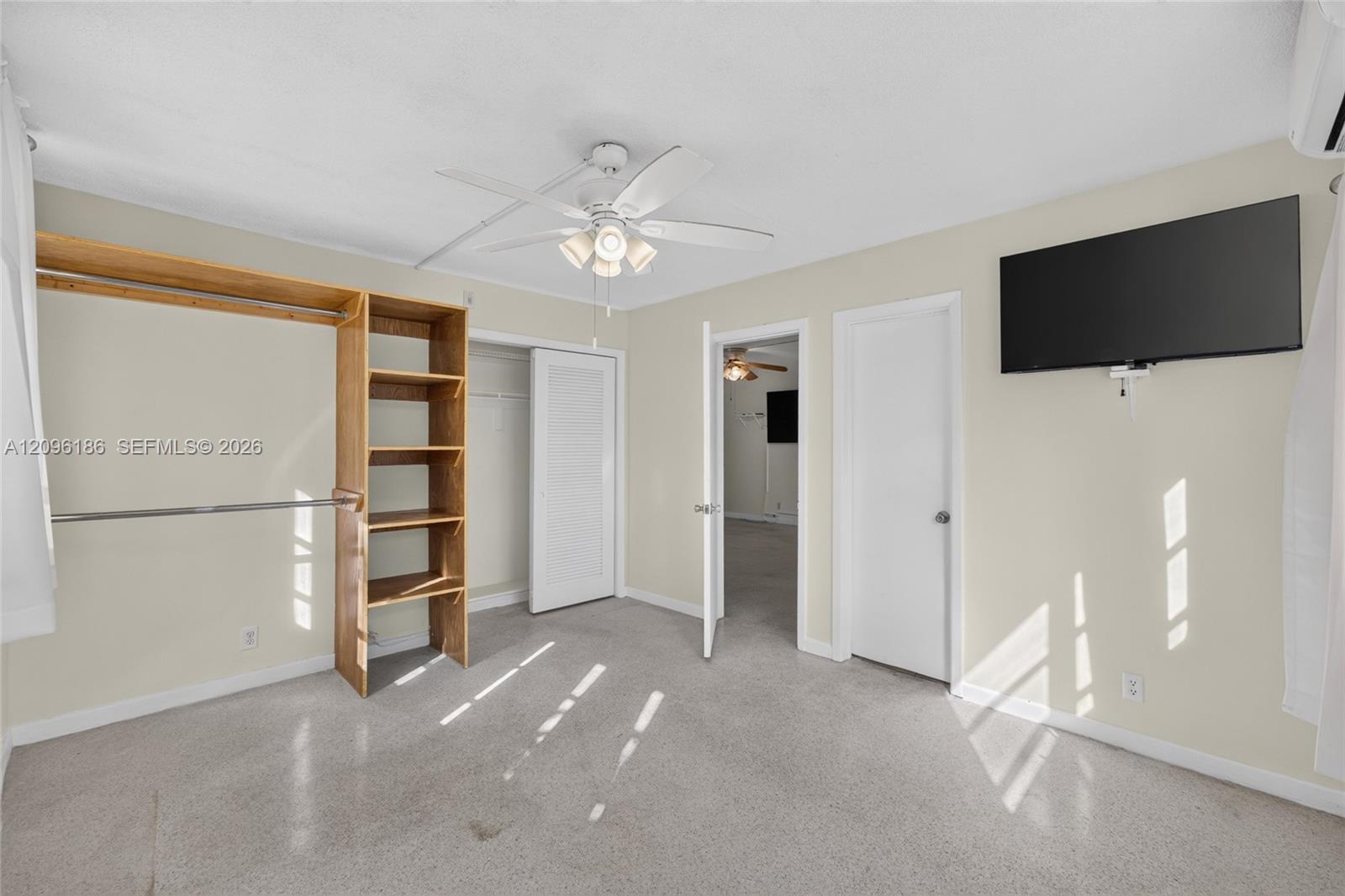 Room featuring neutral wall tones, carpeted flooring, a ceiling fan with integrated lighting, and open-style wood shelving