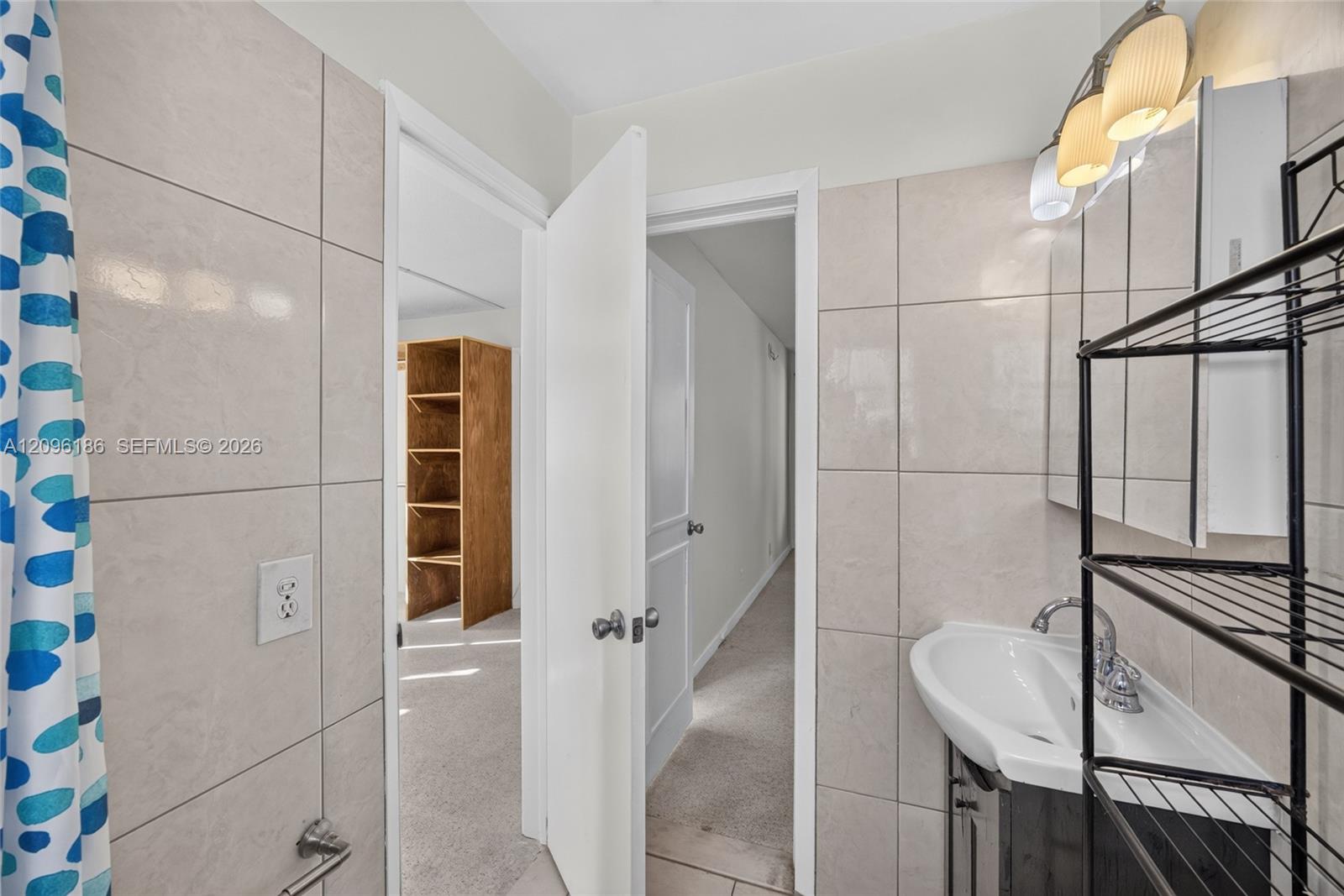 Bathroom featuring large-format ceramic wall tiling, a pedestal sink with a chrome finish faucet, a medicine cabinet with integrated lighting, and built-in shelving