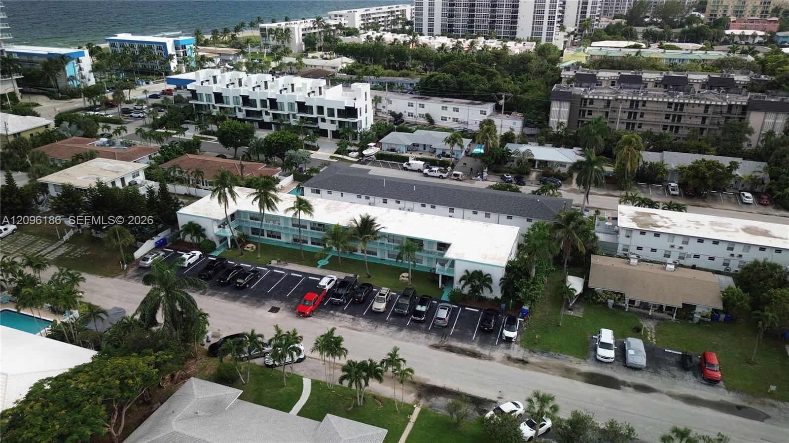 Multi-story residential structure featuring exterior walkways, a dedicated asphalt parking area, and mature palm tree landscaping