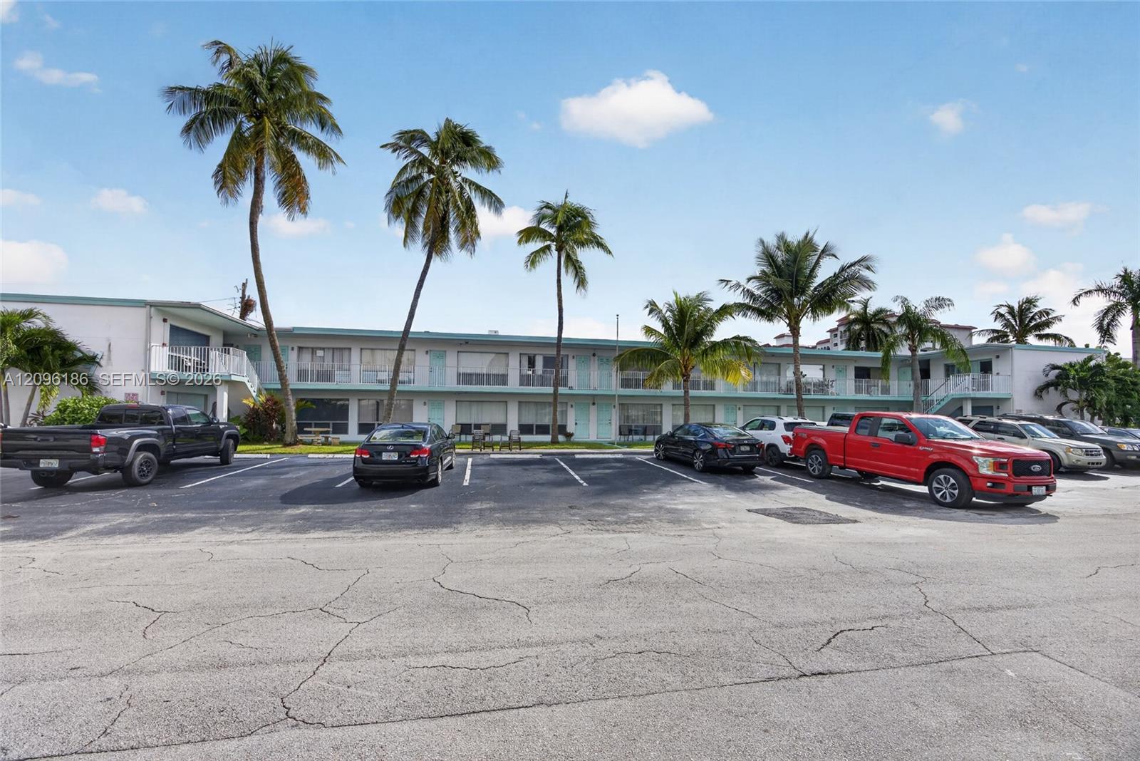Multi-story residential building exterior featuring a white facade, covered walkways with metal railings, and established palm trees Multi-story residential building exterior featuring a white facade, covered walkways with metal railings, and established palm trees