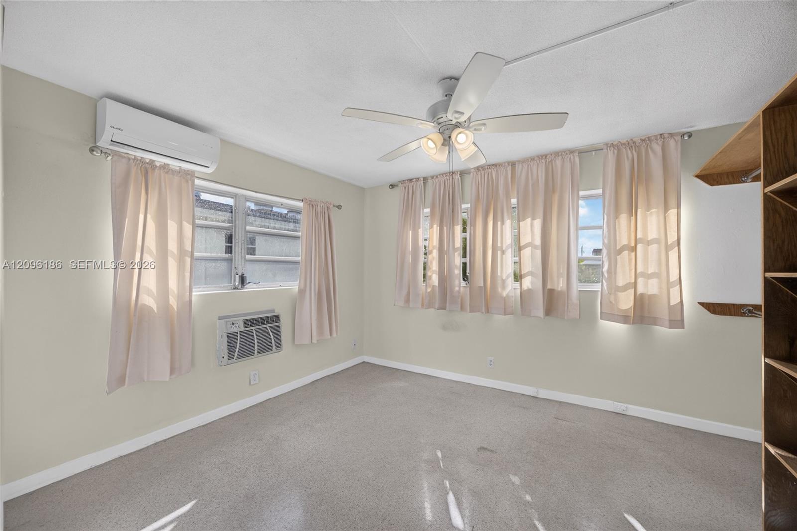 Room featuring a multi-blade ceiling fan with integrated lighting, wall-mounted ductless climate control system, wall-mounted air conditioning unit, and built-in wood shelving