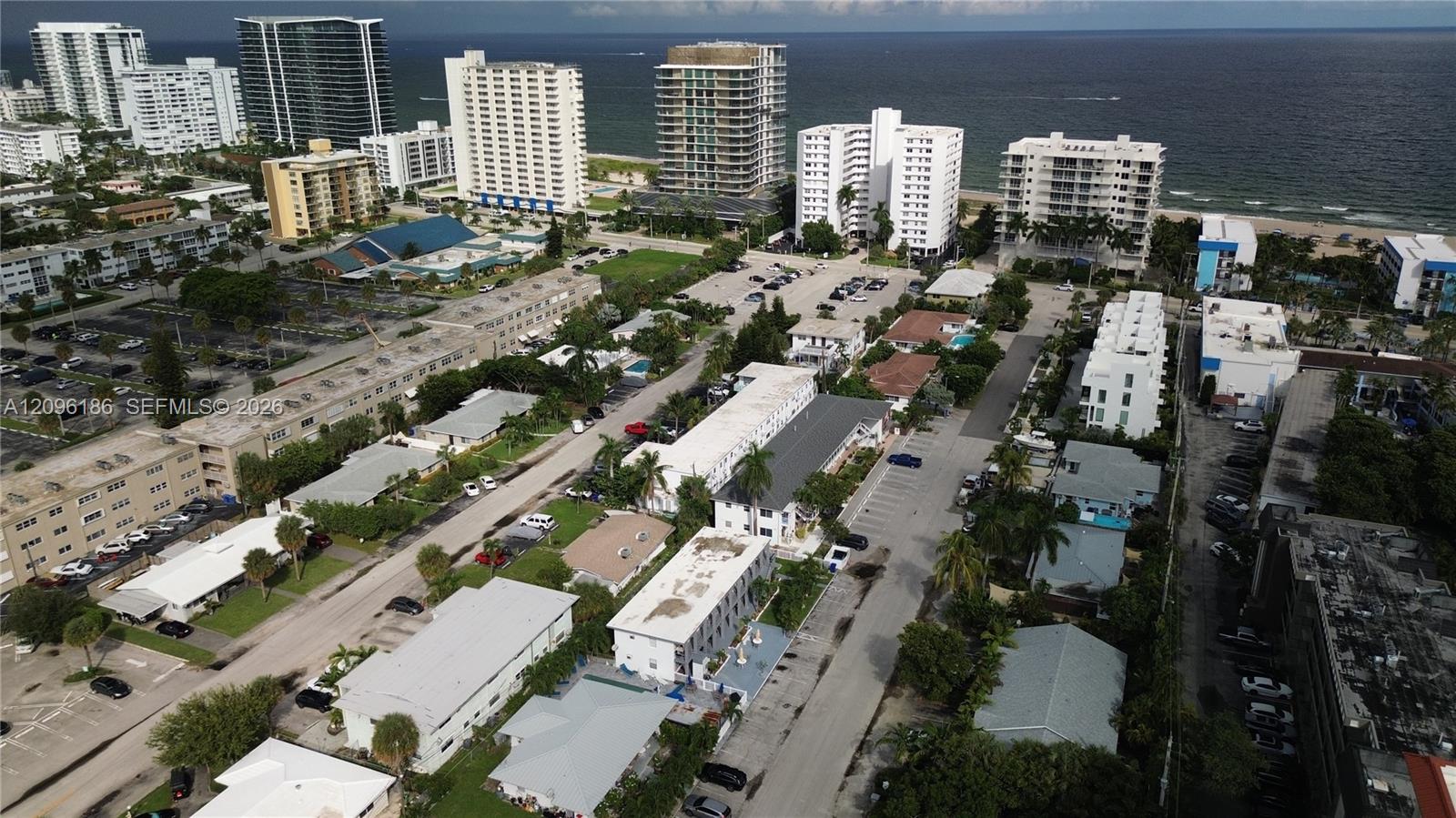 Aerial perspective featuring coastal proximity, multi-story building density, expansive paved parking lots, mature palm trees, and established street-level infrastructure