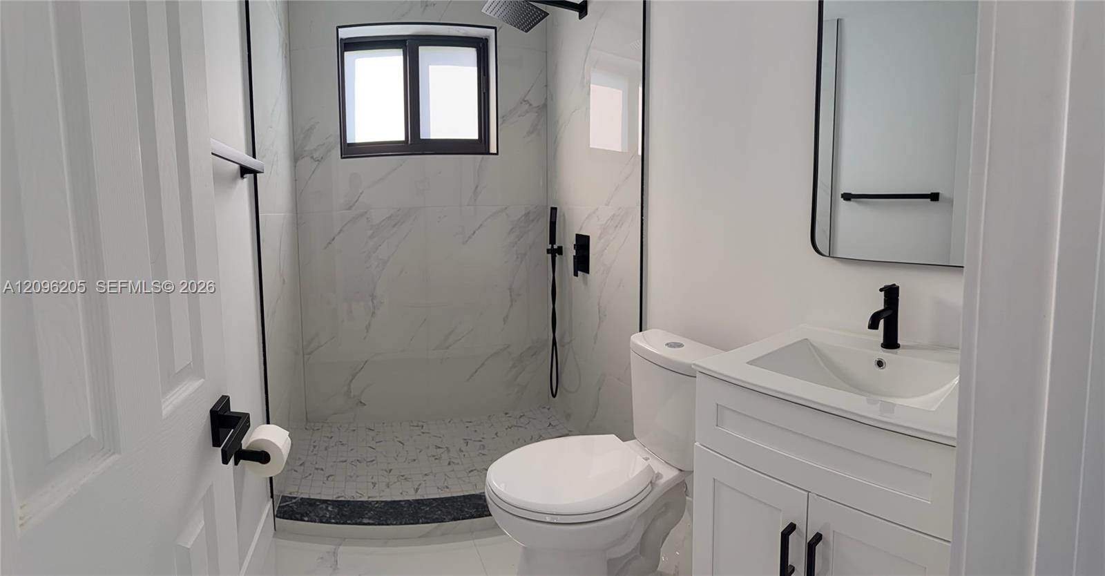 Bathroom featuring a walk-in shower with stone-patterned wall tile, a white vanity with a single basin, a matte black faucet, and a wall-mounted rectangular mirror