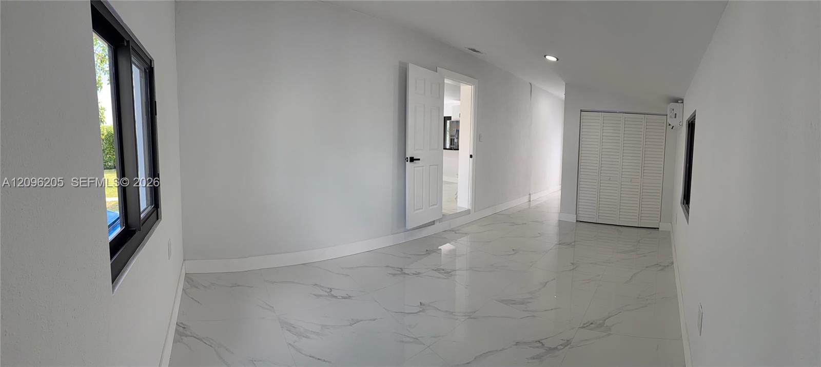 Interior space featuring polished stone-finish tile flooring, recessed ceiling lighting, a closet with white louvered doors, and a six-panel interior door