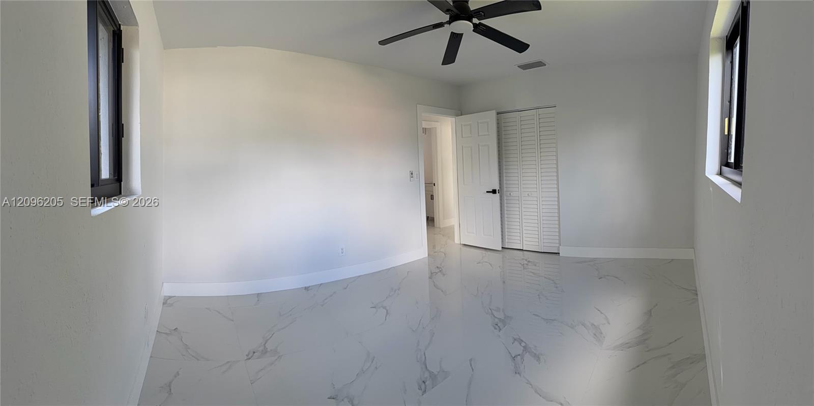 Interior room featuring large-format tile flooring with a neutral veined pattern, dual windows with dark frames, a ceiling fan, and a built-in closet with louvered doors