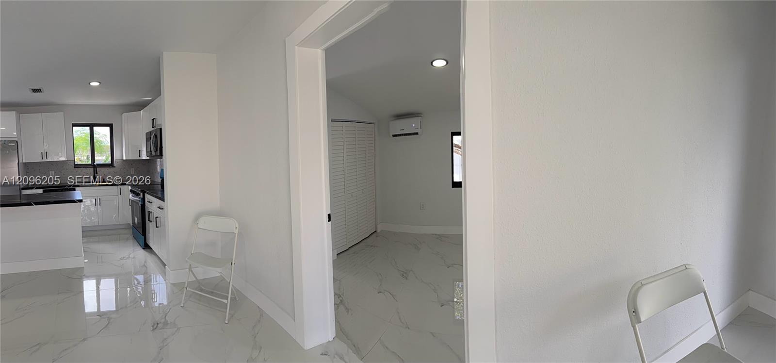 Interior space featuring polished stone-finish tile flooring, white shaker-style cabinetry, dark stone-finish countertops, recessed lighting, and a wall-mounted ductless climate control unit