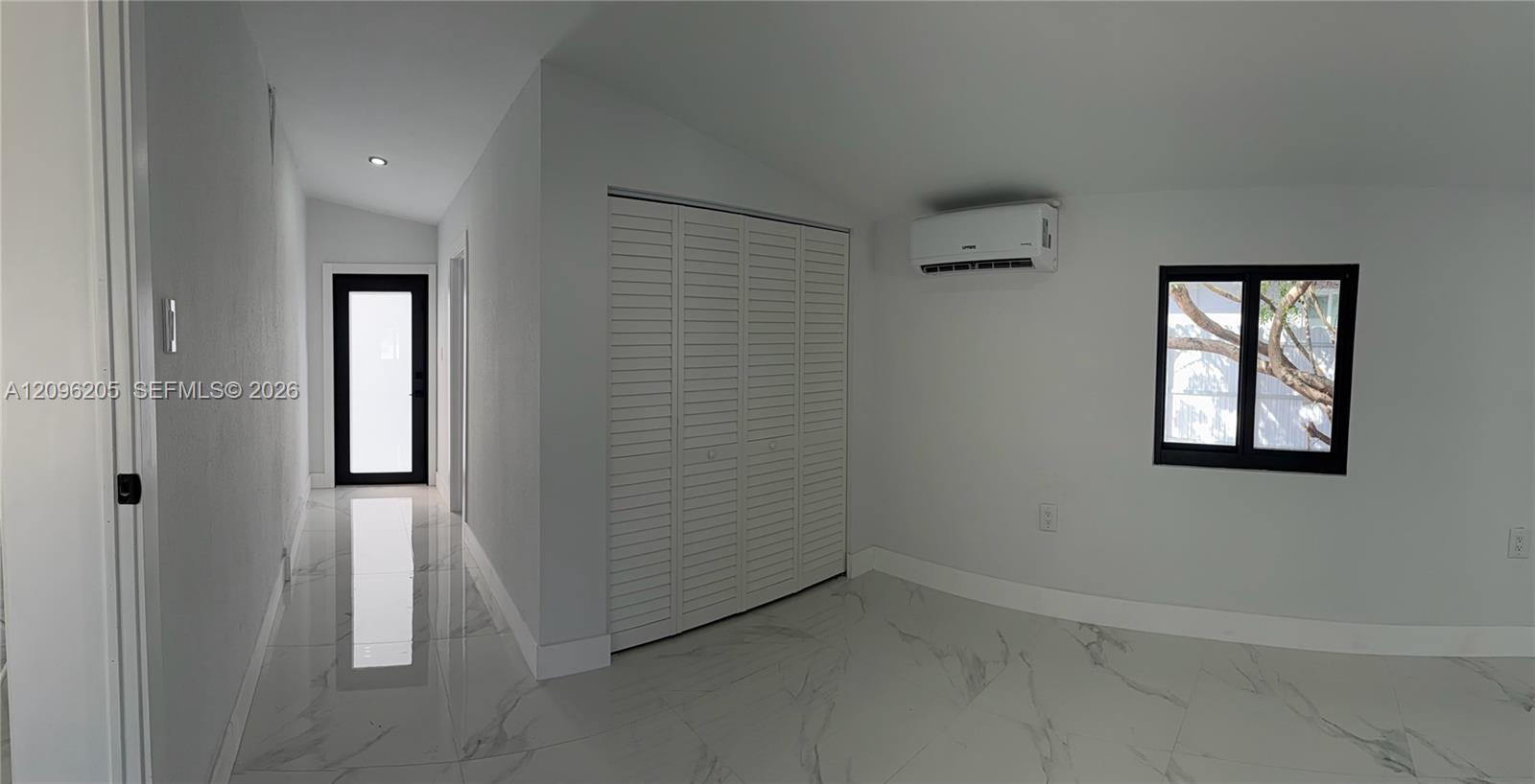 Interior space featuring large-format tile flooring with marble-pattern veining, bifold closet doors, a wall-mounted ductless air conditioning unit, and a black-framed glass-panel door