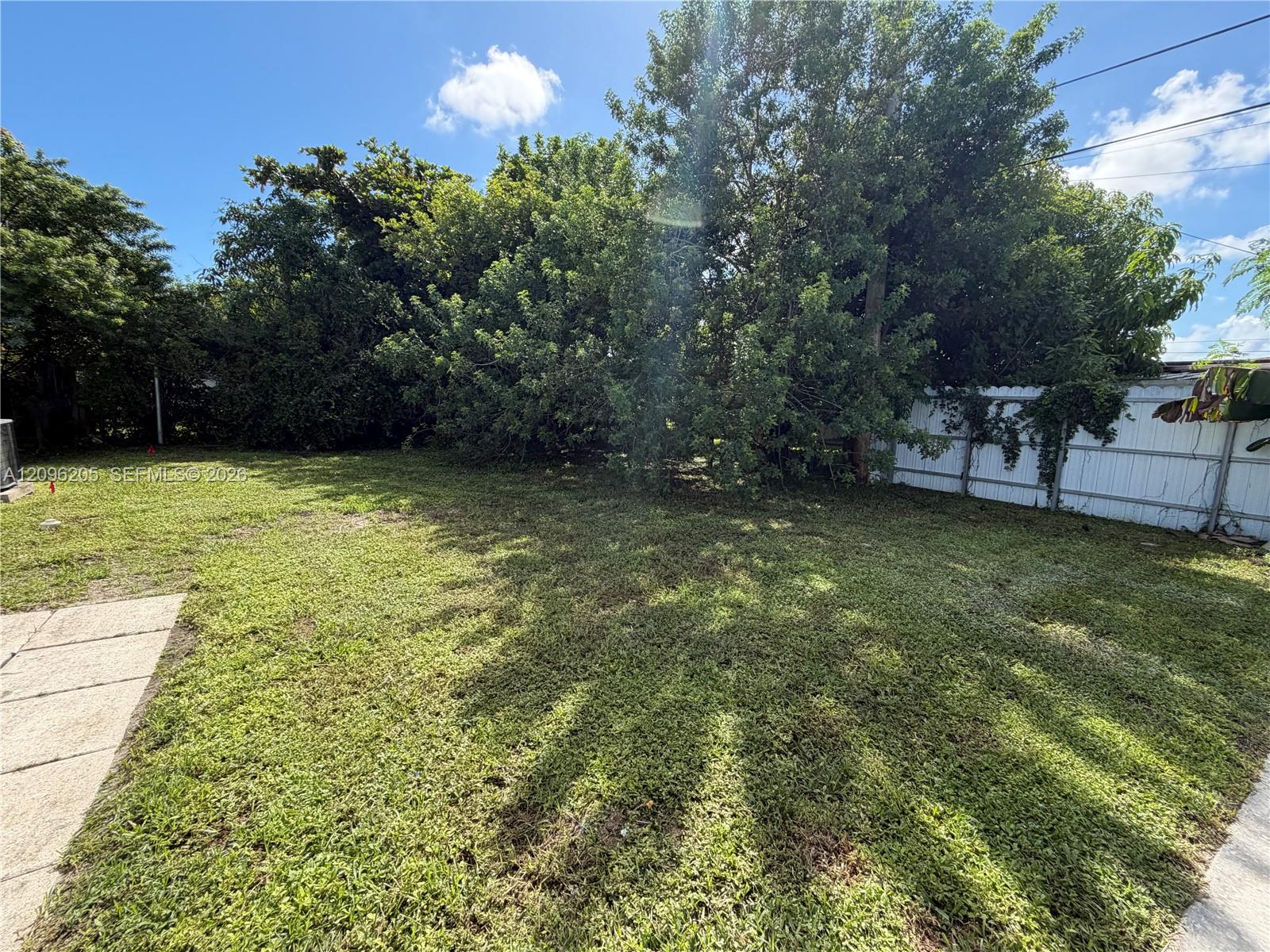 Expansive backyard featuring a large grass lawn, mature trees, and a white privacy fence