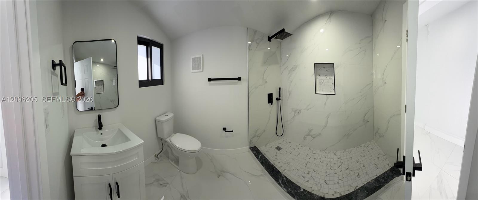Bathroom featuring stone-finish flooring, a vanity with a rectangular sink, matte black hardware, and a walk-in shower with floor-to-ceiling tile surrounds and a built-in recessed niche