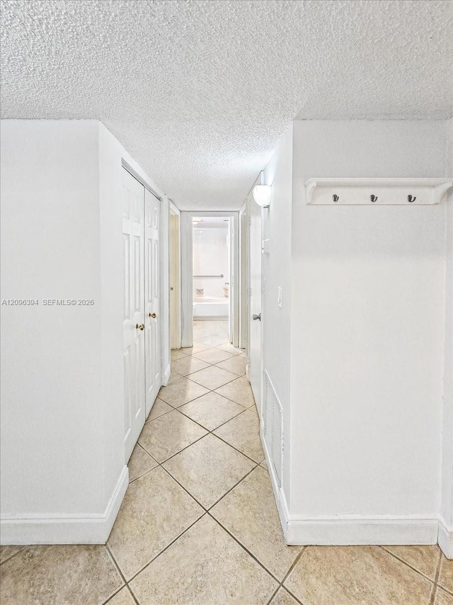 Hallway featuring neutral-toned tile flooring set on a diagonal, dual-panel closet doors, and a wall-mounted hook rack