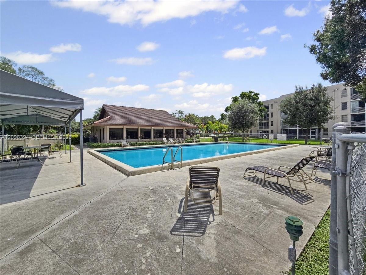 Community swimming pool featuring a concrete deck, covered seating area, and clubhouse