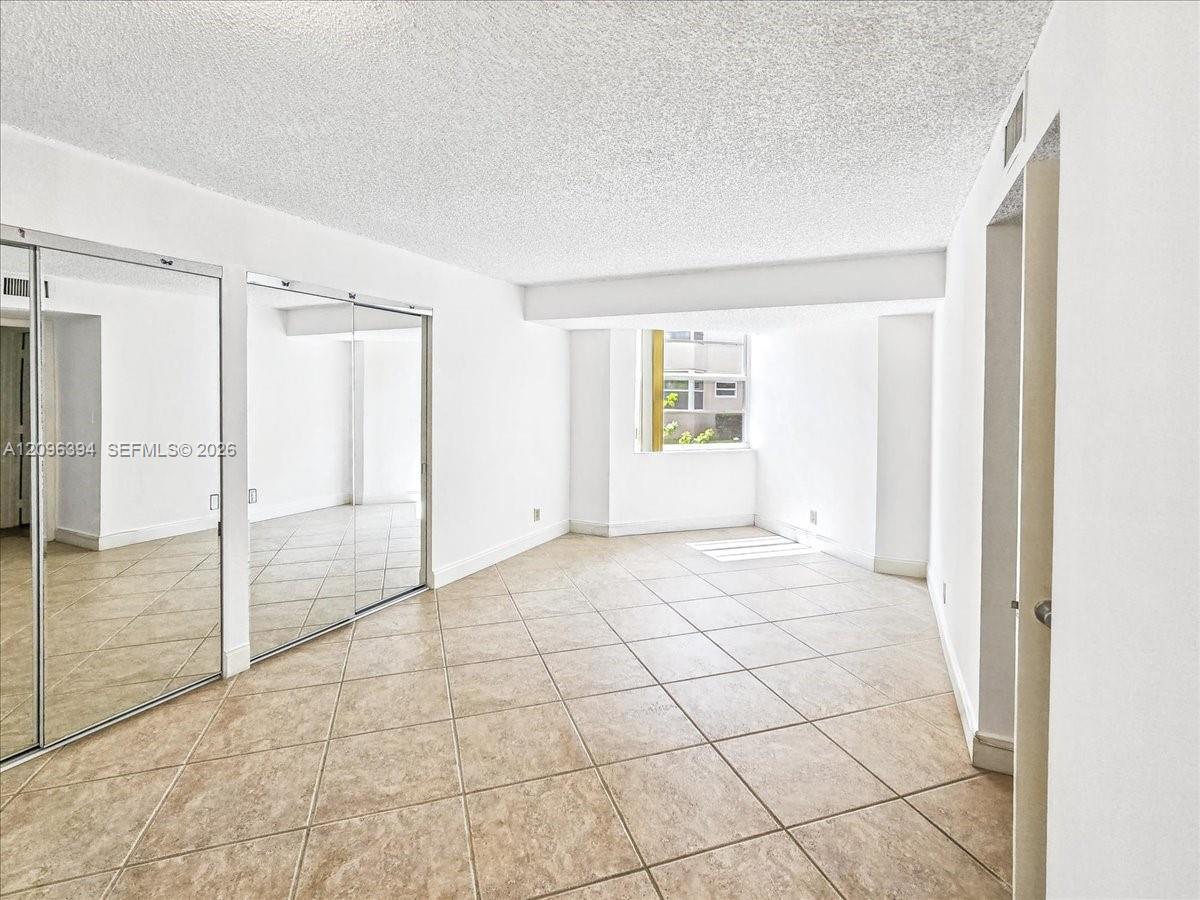 Interior room featuring large-format tile flooring, wall-to-wall mirrored closet doors, and a window providing natural light