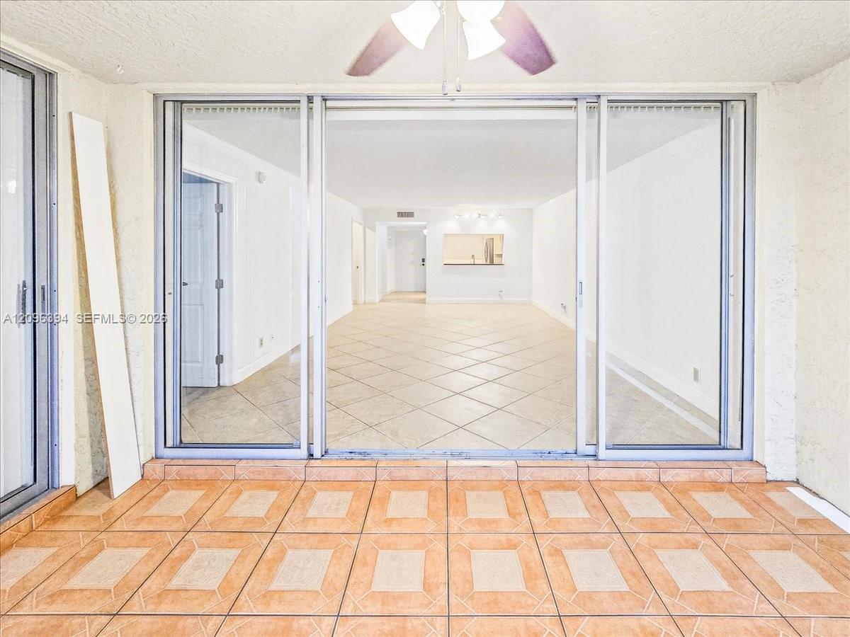 Triple-panel sliding glass doors with brushed metal frames, ceramic tile flooring, and ceiling fan with integrated lighting