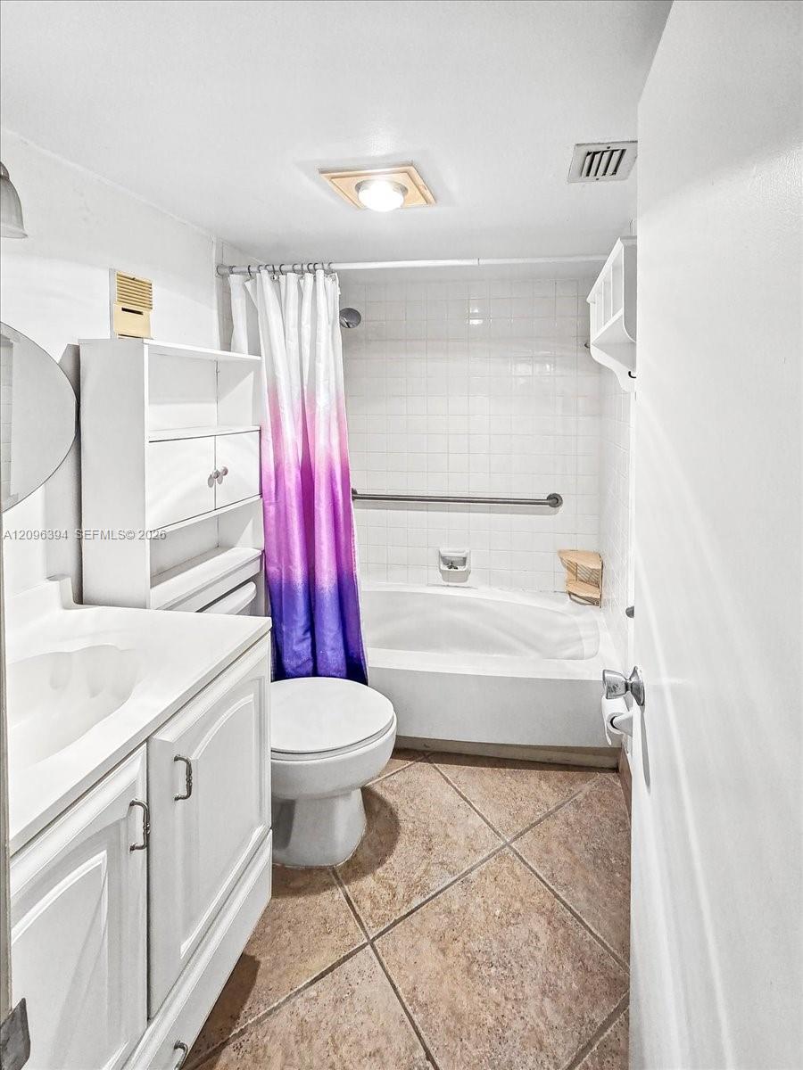 Bathroom featuring tile flooring laid on a diagonal, a white vanity with integrated basin, built-in cabinetry, and a tub with tile surround and wall-mounted grab bar