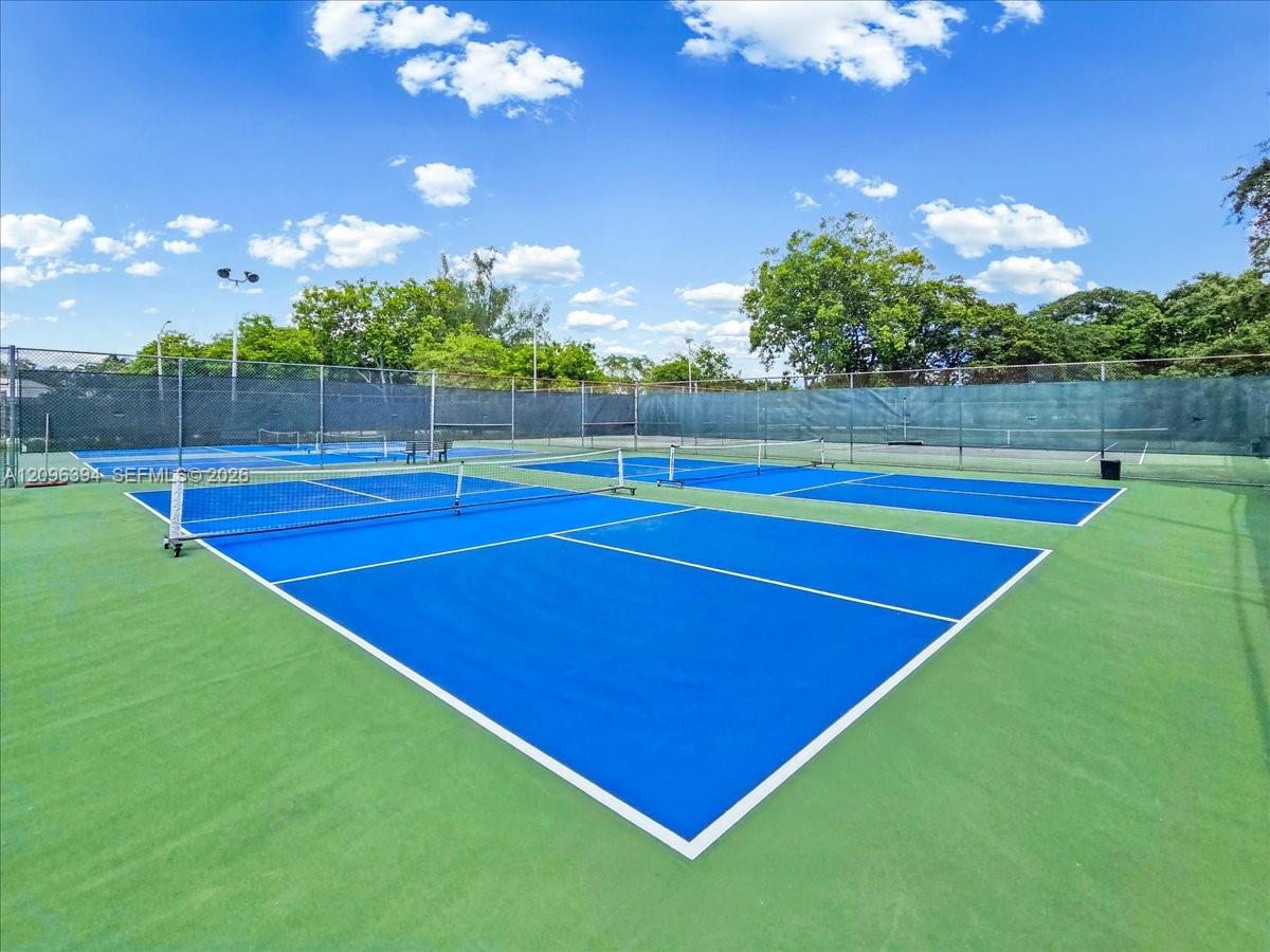 Dual hard-surface courts featuring blue and green painted finishes, white boundary lines, integrated nets, and perimeter chain-link fencing with privacy screening