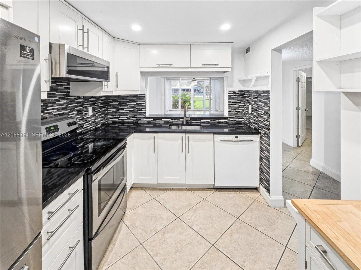 Kitchen featuring white shaker-style cabinetry, dark stone countertops, decorative multi-tonal backsplash, stainless steel appliances, and ceramic tile flooring