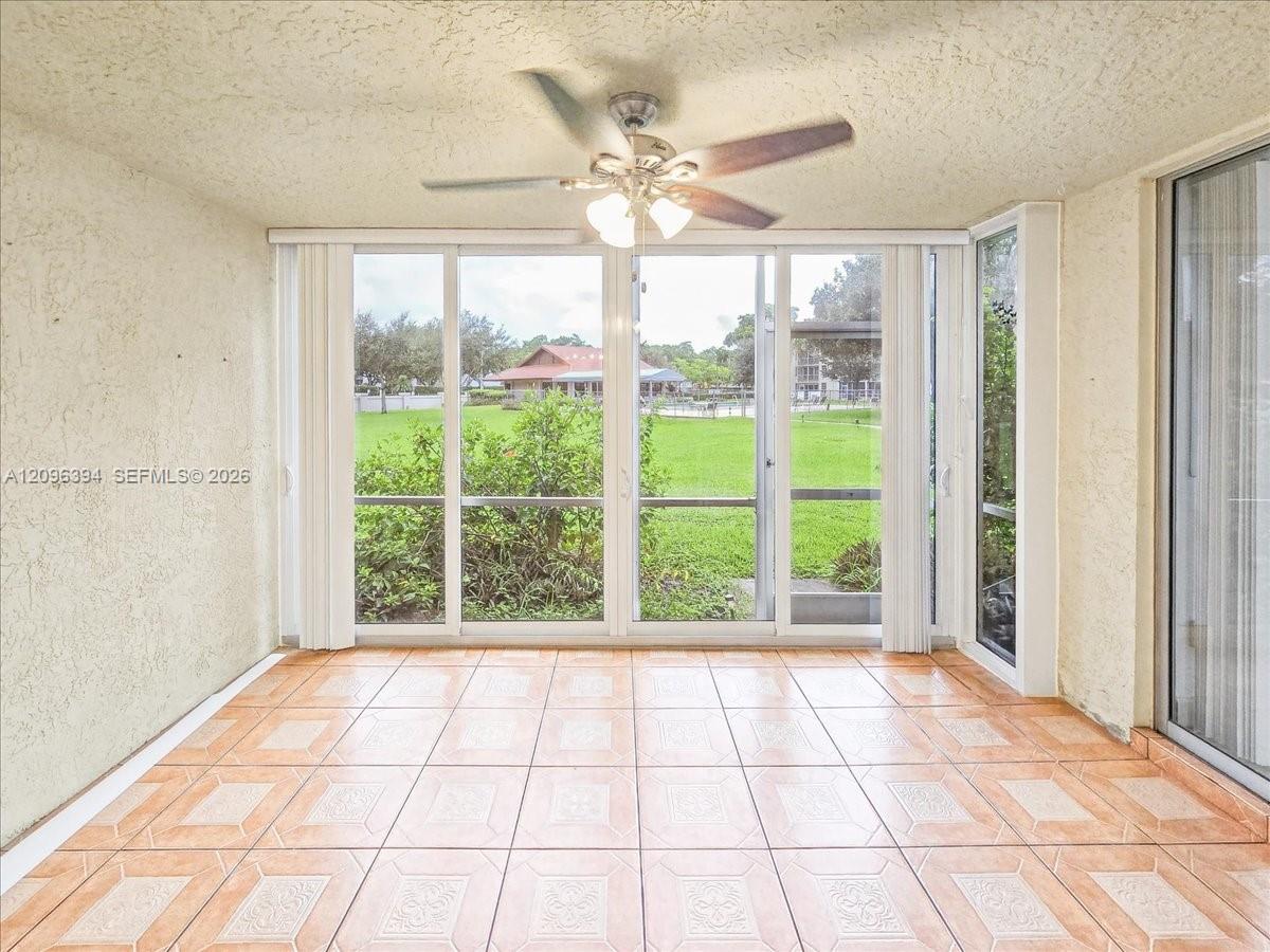 Enclosed sunroom featuring ceramic tile flooring, textured ceilings, a multi-blade ceiling fan with integrated lighting, and expansive glass sliding door panels