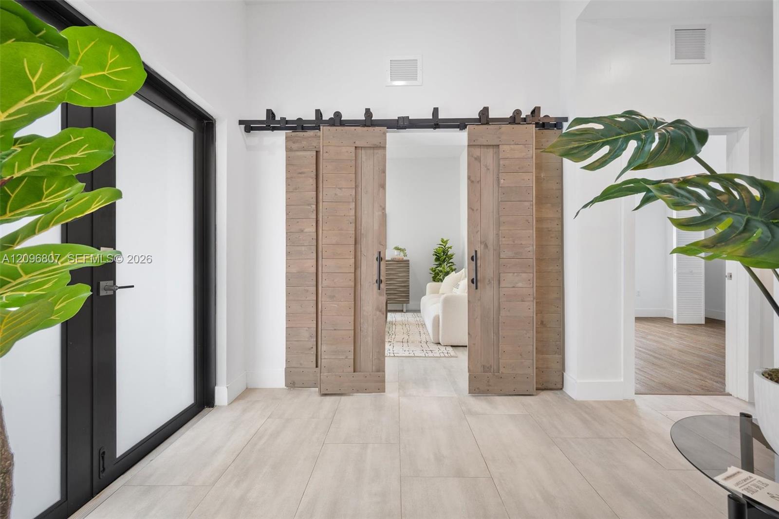 Double sliding barn doors with a matte black metal track system, wood-finish flooring, and black-framed glass entry door Double sliding barn doors with a matte black metal track system, wood-finish flooring, and black-framed glass entry door