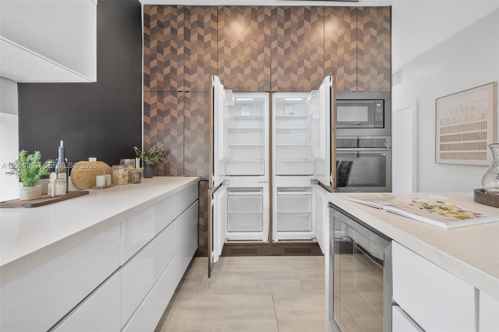 Modern kitchen featuring full-height geometric patterned cabinetry, integrated side-by-side refrigerator, built-in stainless steel oven and microwave, matte white flat-panel cabinetry, and solid surface countertops
