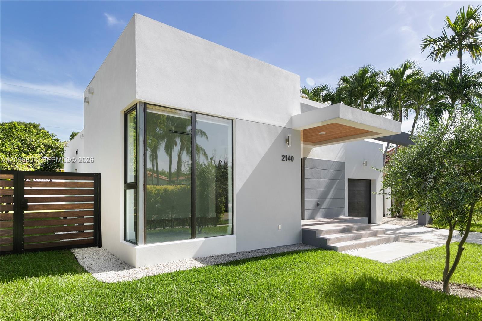 Modern exterior featuring a smooth stucco finish, floor-to-ceiling corner glazing, a wood-paneled cantilevered entryway, horizontal slat fencing, and concrete step entrance Modern exterior featuring a smooth stucco finish, floor-to-ceiling corner glazing, a wood-paneled cantilevered entryway, horizontal slat fencing, and concrete step entrance