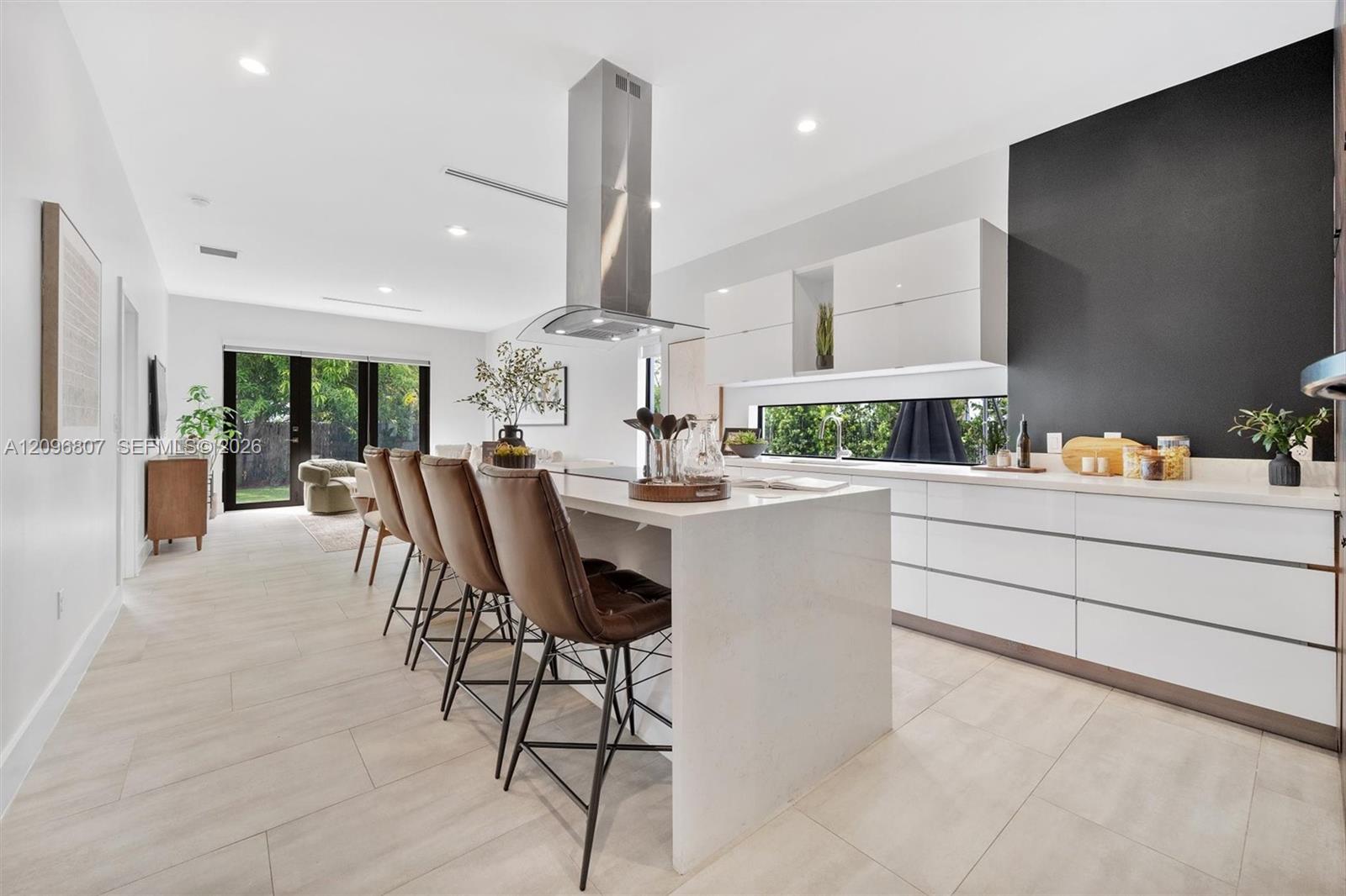 Kitchen featuring a large central island with quartz countertops, minimalist high-gloss white cabinetry, a stainless steel chimney-style range hood, and porcelain tile flooring Kitchen featuring a large central island with quartz countertops, minimalist high-gloss white cabinetry, a stainless steel chimney-style range hood, and porcelain tile flooring