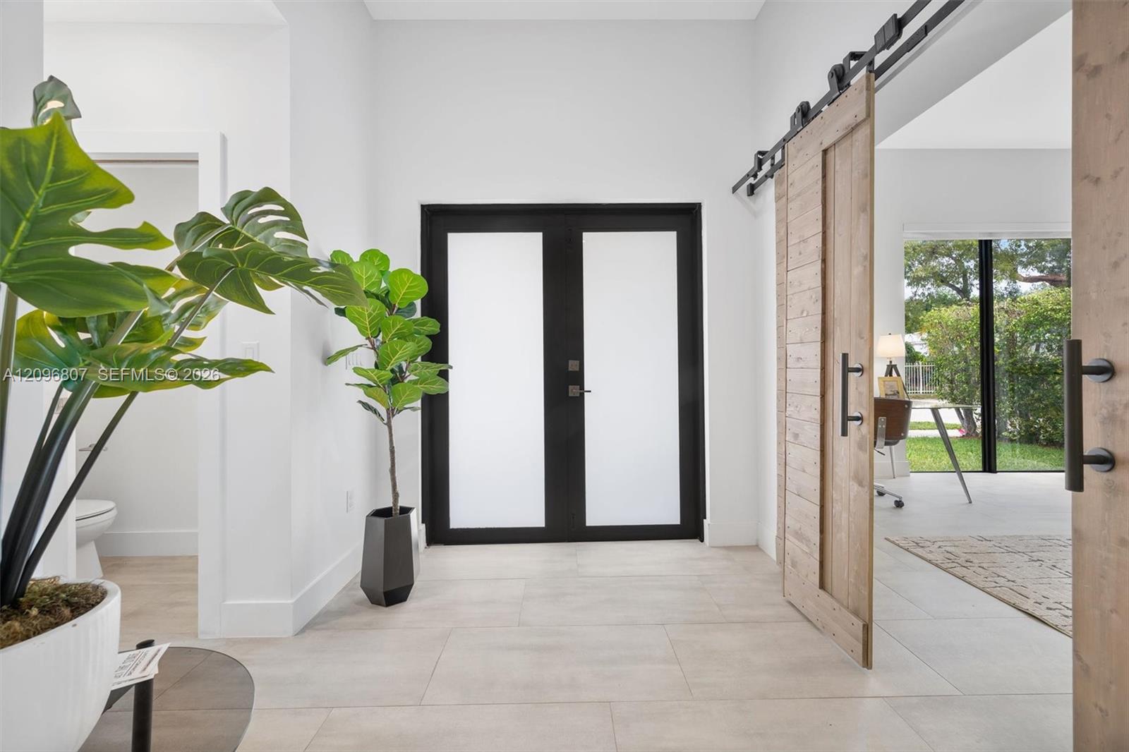 Entryway featuring double doors with frosted glass insets, large-format tile flooring, and wood-finish sliding barn doors with black metal hardware Entryway featuring double doors with frosted glass insets, large-format tile flooring, and wood-finish sliding barn doors with black metal hardware
