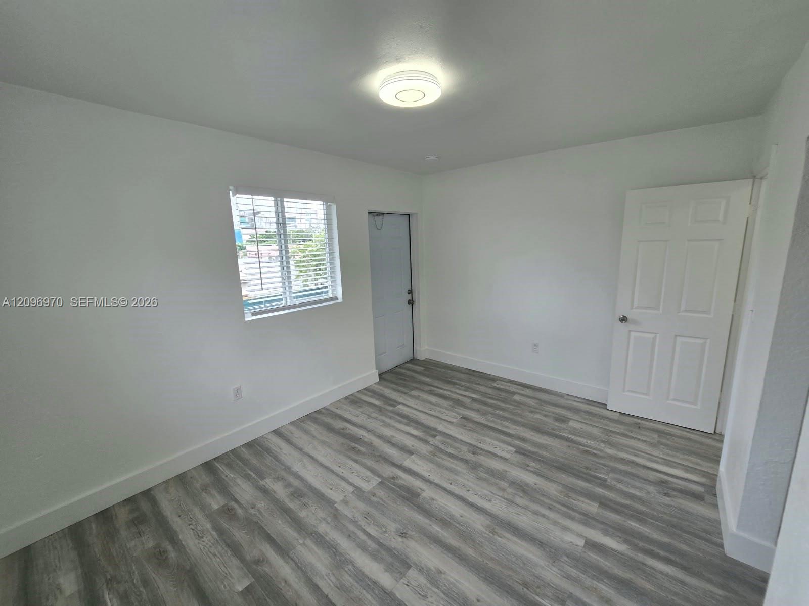 Interior space featuring neutral wall paint, wood-finish flooring, a flush-mount circular ceiling light, a multi-pane window, and a six-panel door
