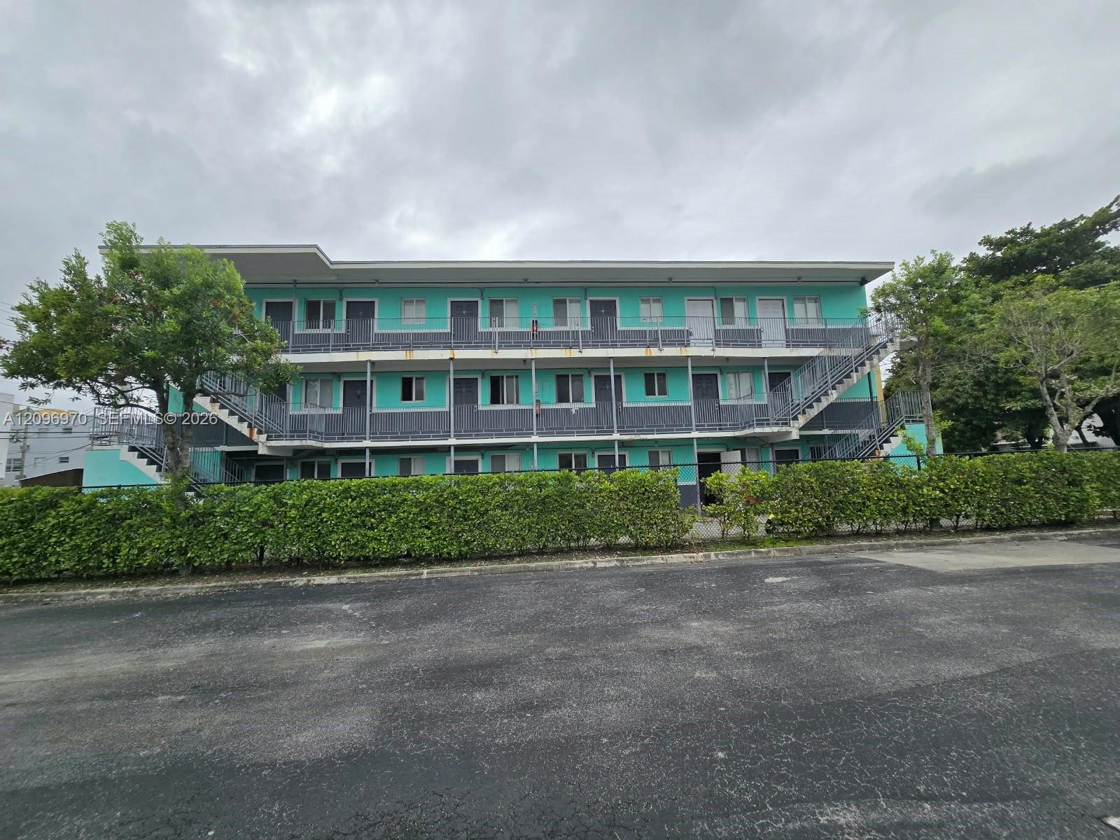 Multi-story building exterior featuring a teal and gray facade, metal staircases, exterior walkways, and mature landscaping Multi-story building exterior featuring a teal and gray facade, metal staircases, exterior walkways, and mature landscaping
