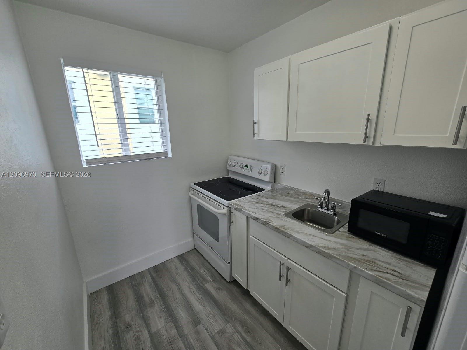 Kitchen featuring white shaker-style cabinetry, stone-patterned laminate countertops, stainless steel sink with pull-out faucet, and wood-finish flooring Kitchen featuring white shaker-style cabinetry, stone-patterned laminate countertops, stainless steel sink with pull-out faucet, and wood-finish flooring