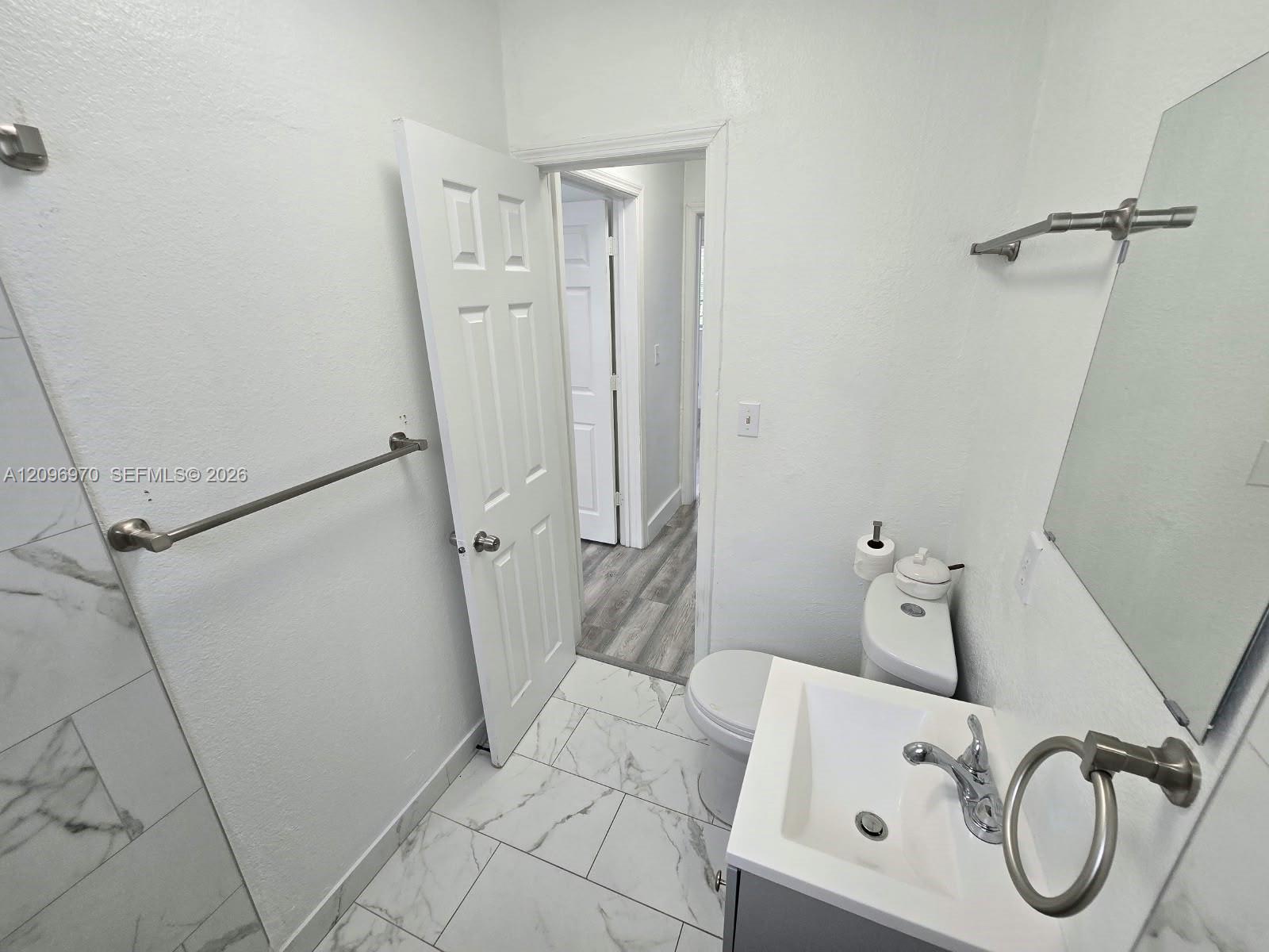 Bathroom featuring large-format tile flooring with a marble-finish, a vanity with a white rectangular basin and metal fixtures, and a shower surround with marble-finish tiling