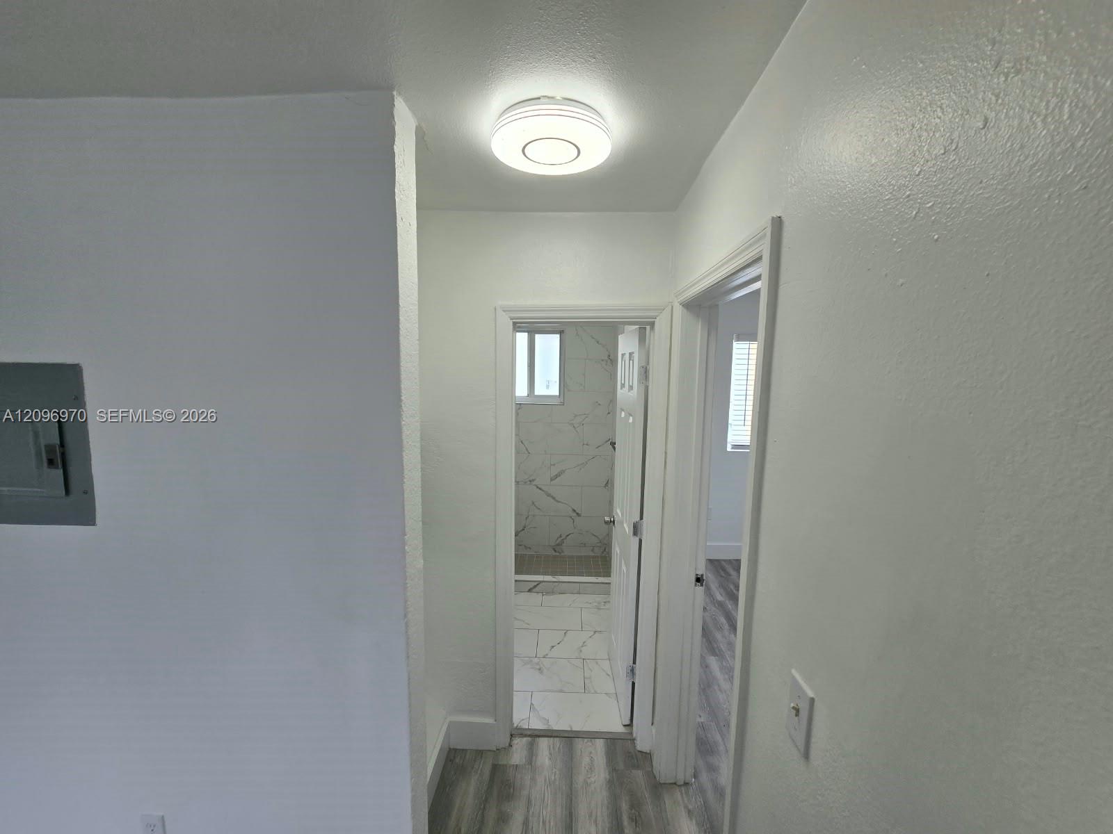 Flush-mount LED ceiling lighting, wood-finish flooring, and a bathroom featuring large-format tile flooring and wall surfacing