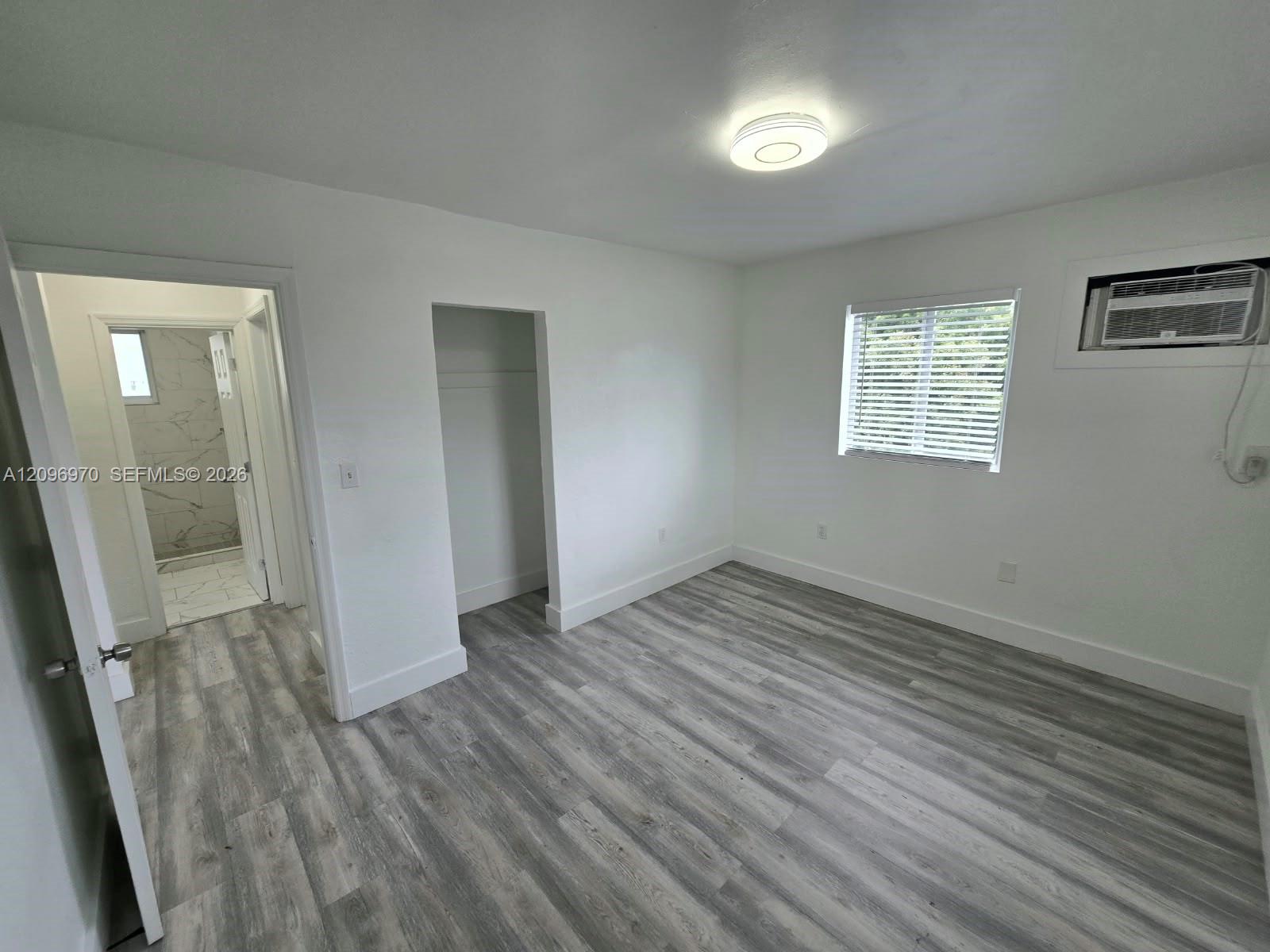 Room featuring wood-finish flooring, recessed LED lighting, a window with horizontal blinds, and a built-in wall air conditioning unit