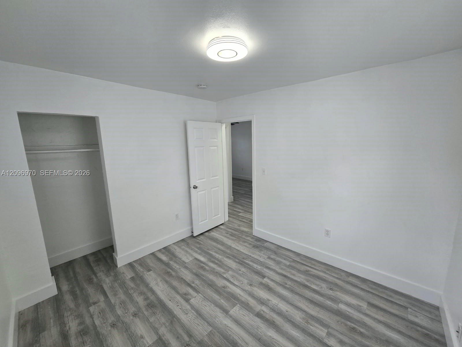 Neutral interior room featuring wood-finish flooring, a six-panel interior door, a built-in closet with overhead shelving, and a circular flush-mount ceiling light fixture