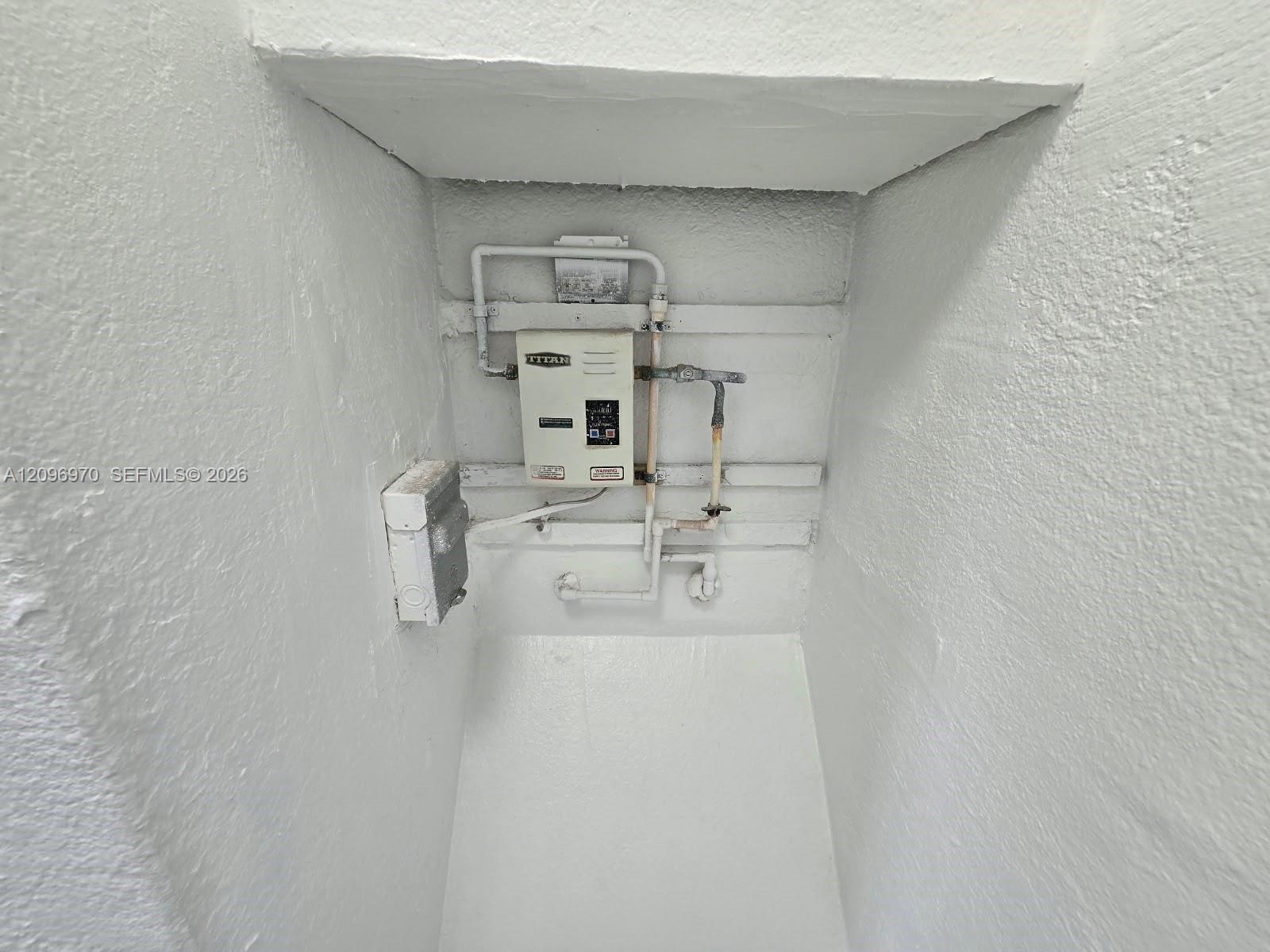 Electric tankless water heater with dedicated electrical disconnect and exposed plumbing conduits housed within a recessed utility alcove