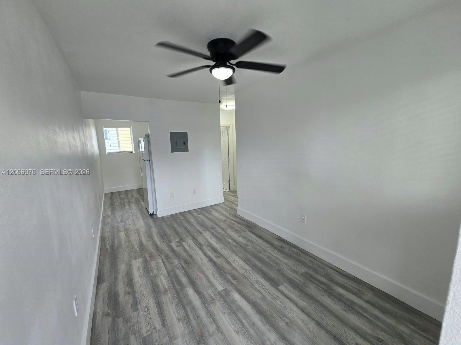 Interior space featuring wood-finish flooring, white walls, and a ceiling fan with integrated lighting Interior space featuring wood-finish flooring, white walls, and a ceiling fan with integrated lighting