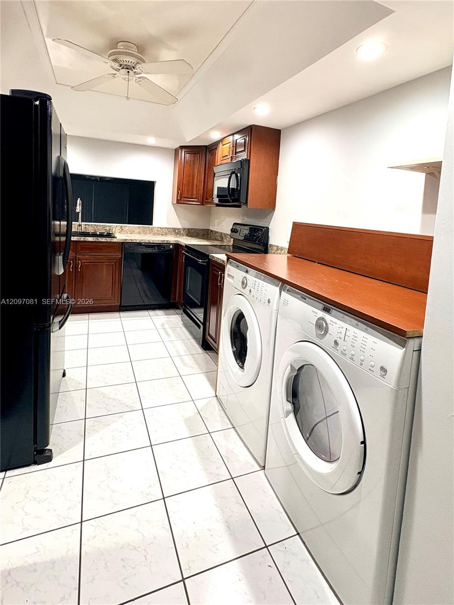 Kitchen featuring wood cabinetry, stone-finish countertops, tile flooring, built-in black appliances, and laundry area with an integrated wood-surface folding counter