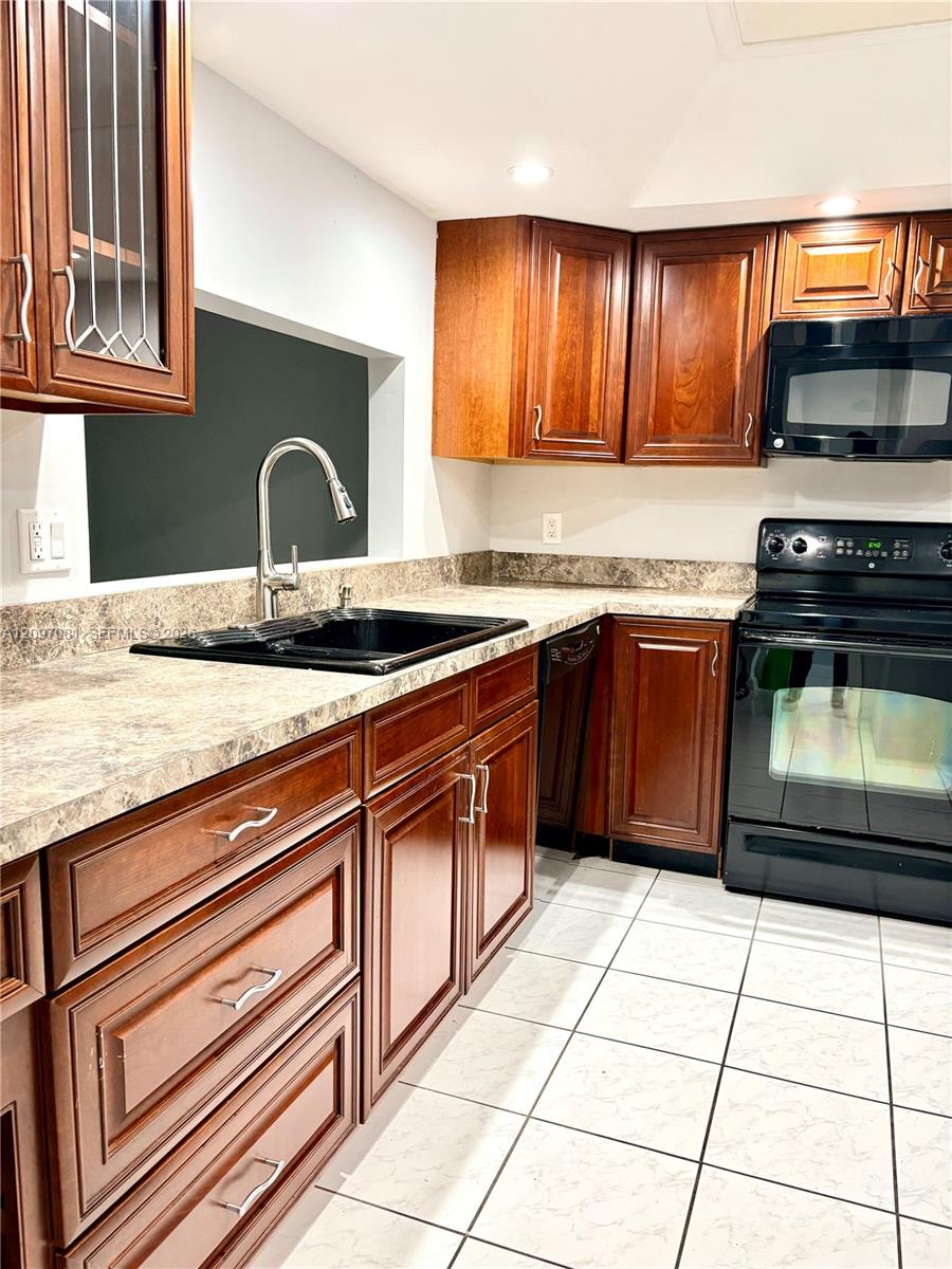 Kitchen featuring warm-tone wood cabinetry, black integrated appliances, a high-arc pull-down faucet, and neutral laminate countertops