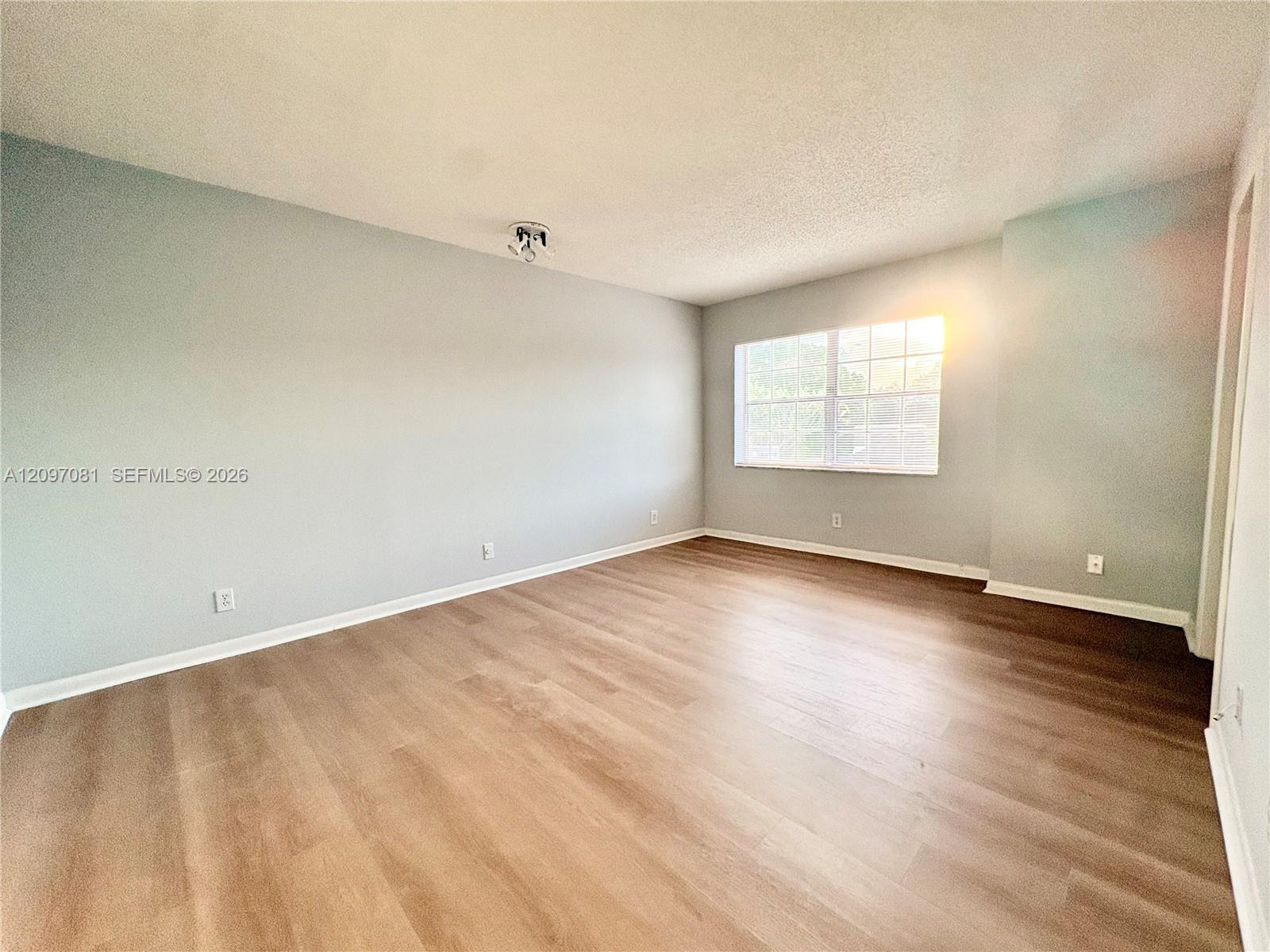 Neutral-toned interior space featuring wood-finish flooring, multi-pane window, and overhead ceiling-mounted lighting