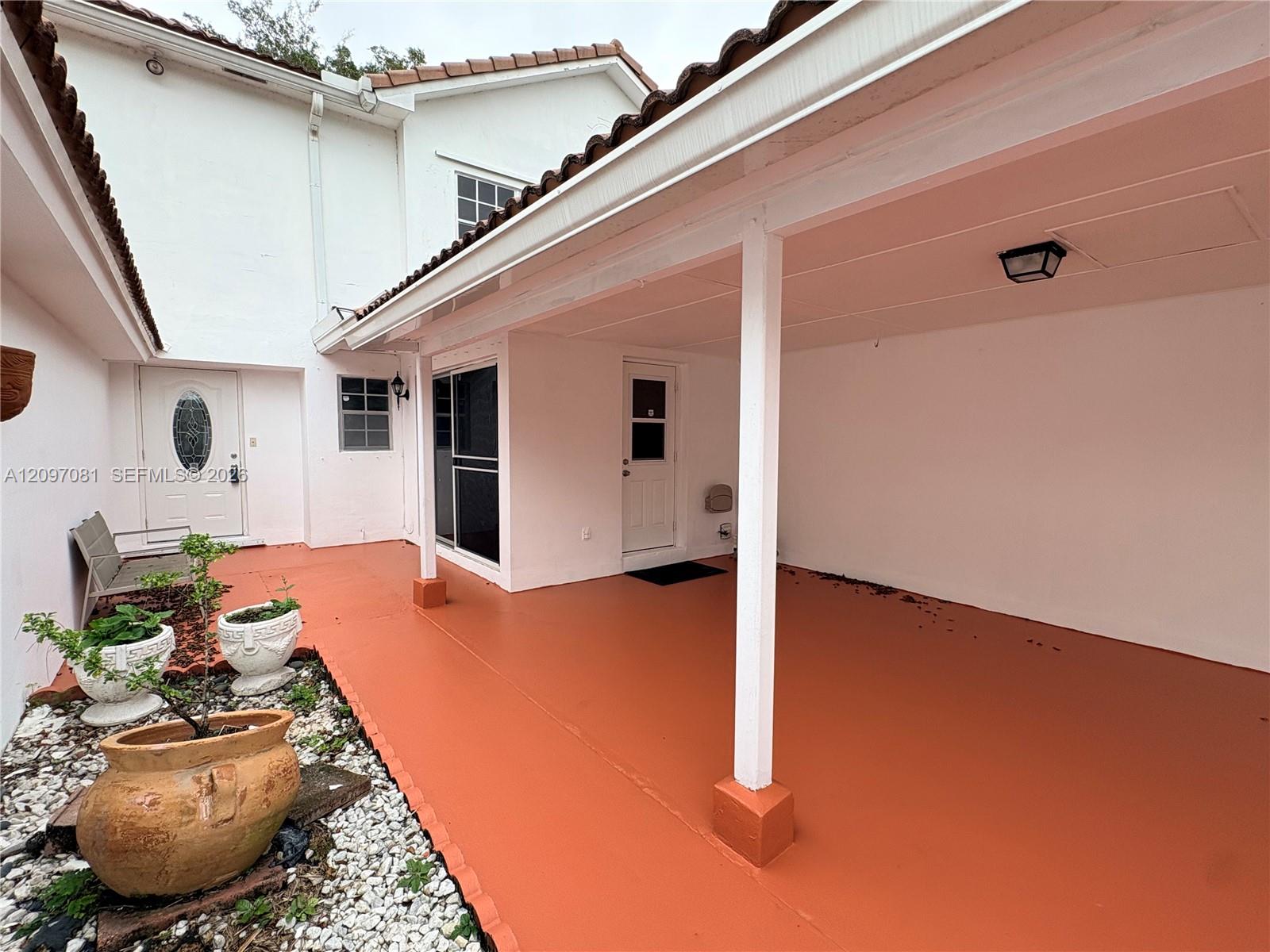Covered patio featuring a solid-surface floor, two exterior entry doors, and a gravel-lined landscape bed