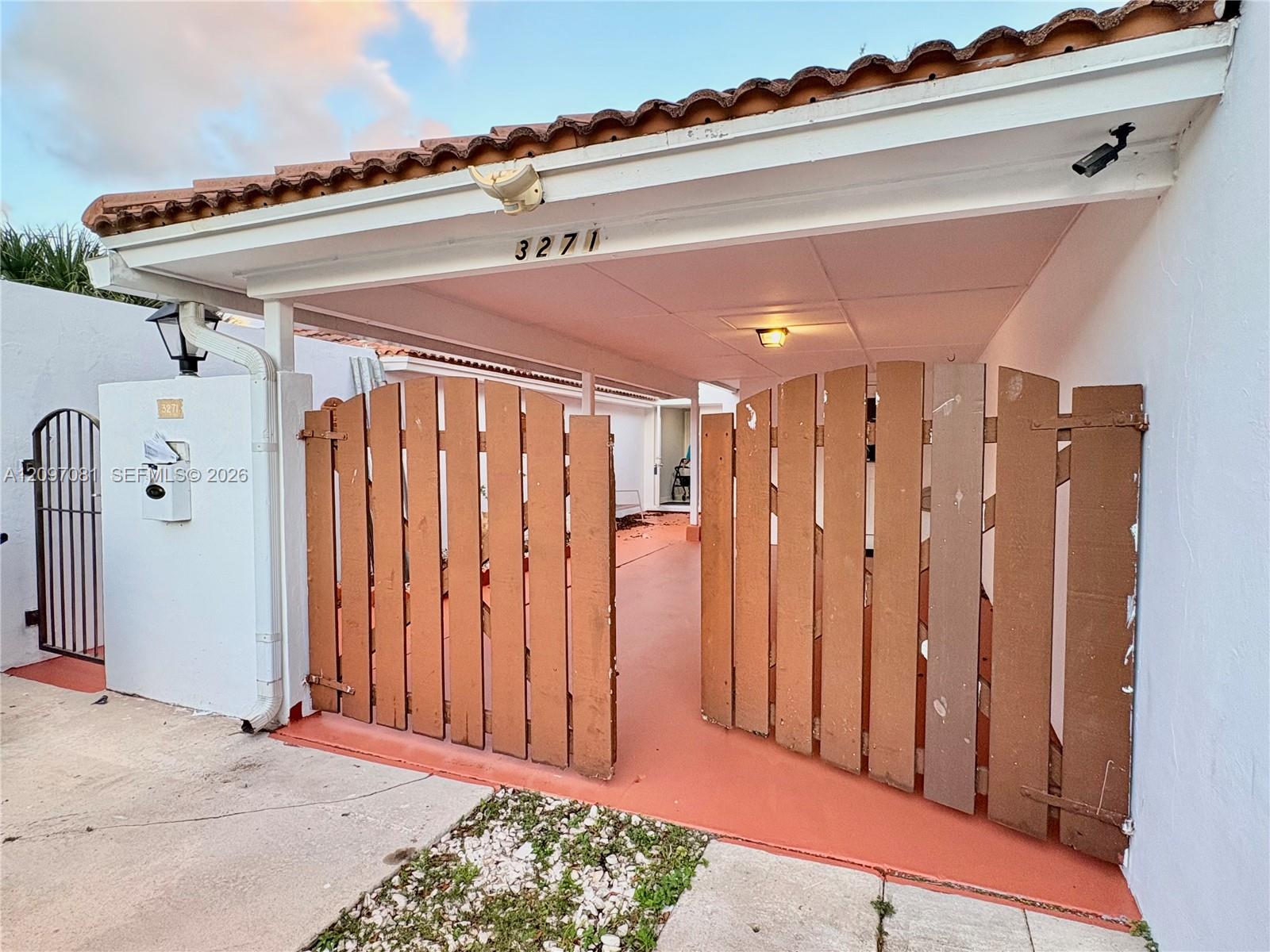 Covered carport featuring a terracotta-tiled roof, privacy-style wood fencing, and a supplemental metal gate entry Covered carport featuring a terracotta-tiled roof, privacy-style wood fencing, and a supplemental metal gate entry