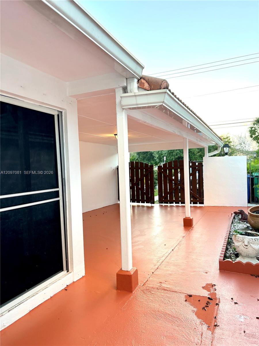 Covered patio featuring a painted concrete surface, support columns, a sliding glass door, and a decorative garden border