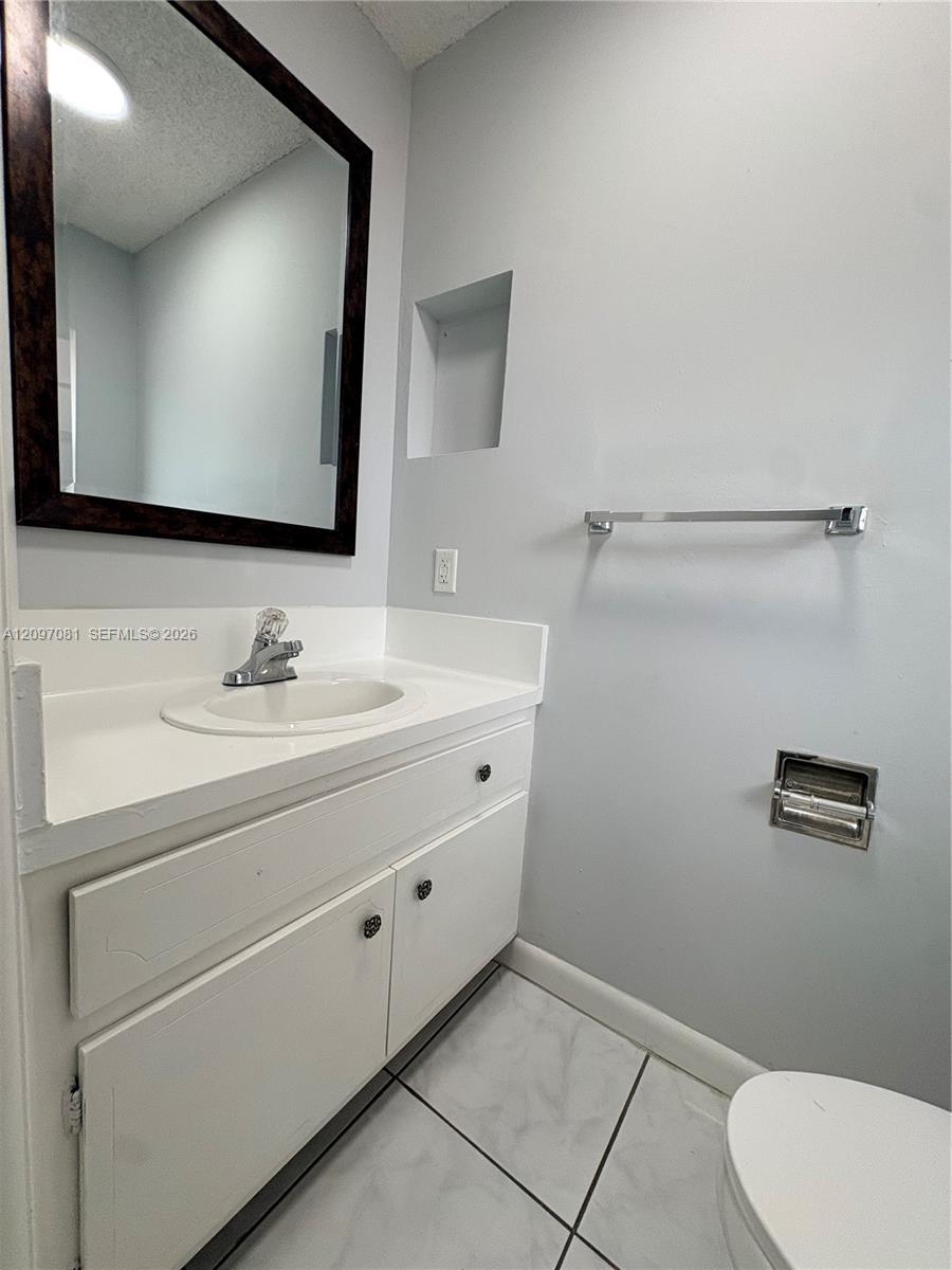 White vanity featuring an integrated basin and solid-surface countertop, paired with a dark-frame wall mirror, recessed wall niche, and ceramic tile flooring