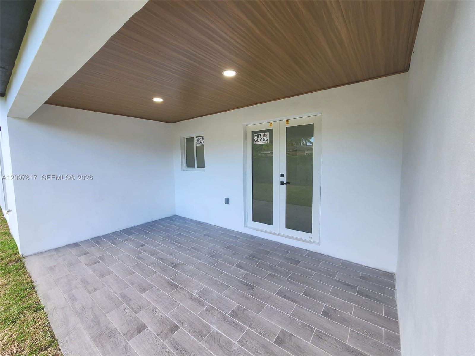 Covered patio featuring wood-finish ceiling paneling, recessed lighting, white exterior walls, and gray stone-finish tile flooring with double glass doors