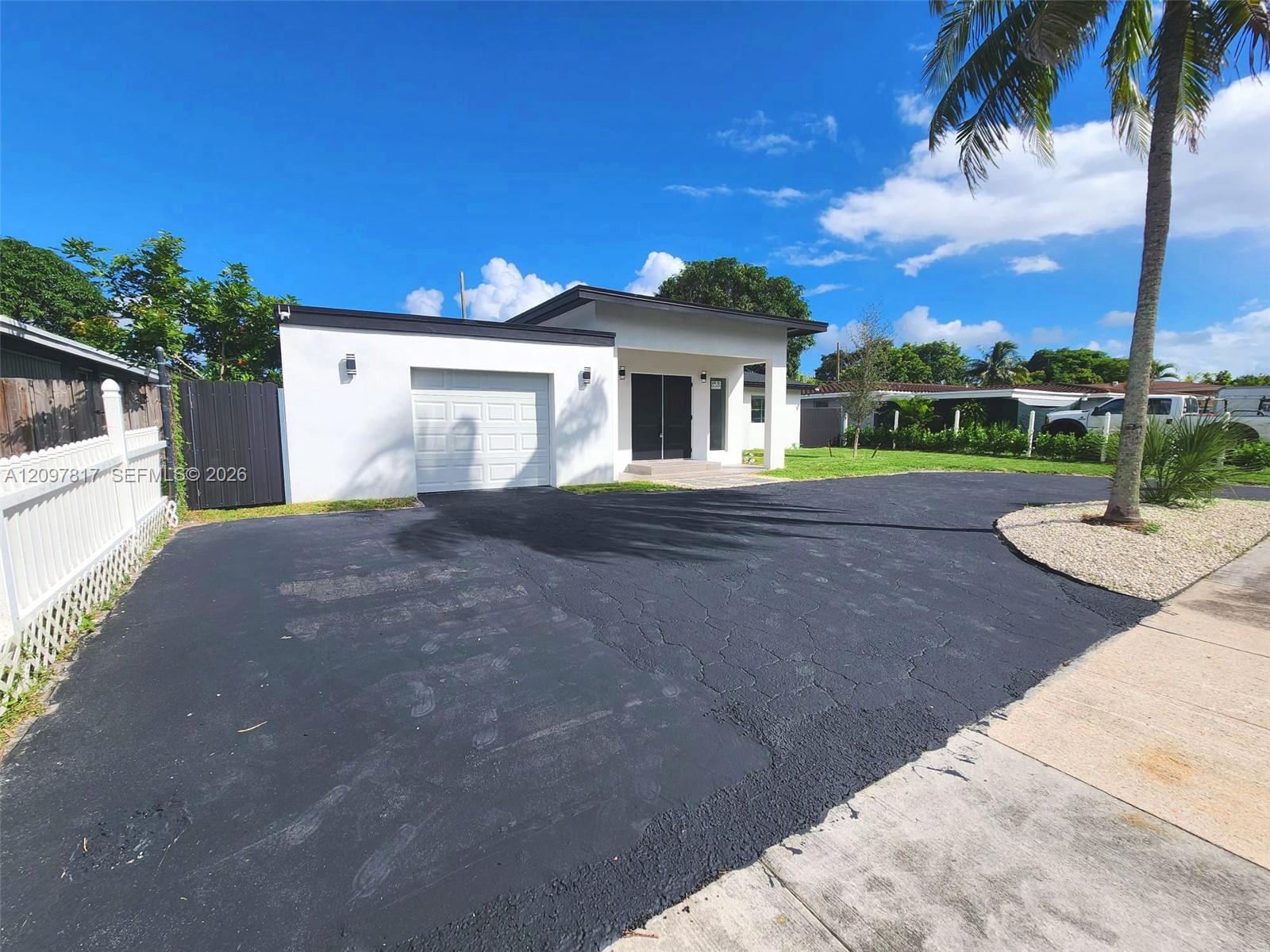 Contemporary exterior featuring a flat roofline, paved driveway, attached garage, and white perimeter fencing
